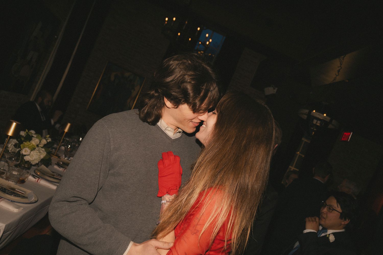 Couple sharing romantic kiss at dimly lit wedding reception dinner table.