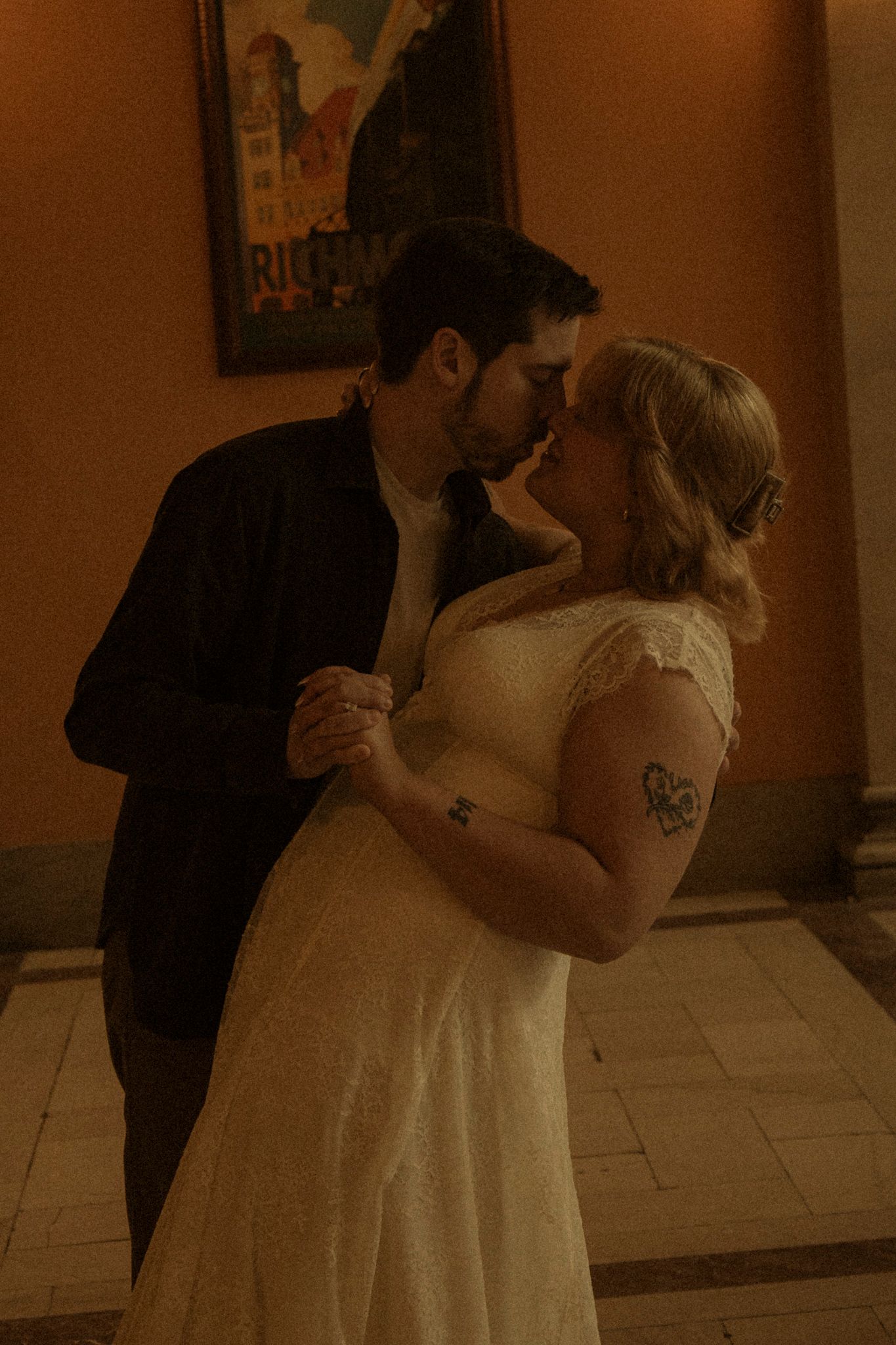 Two people share an intimate dance in an elegant corridor with tiled floors and warm ambient lighting.