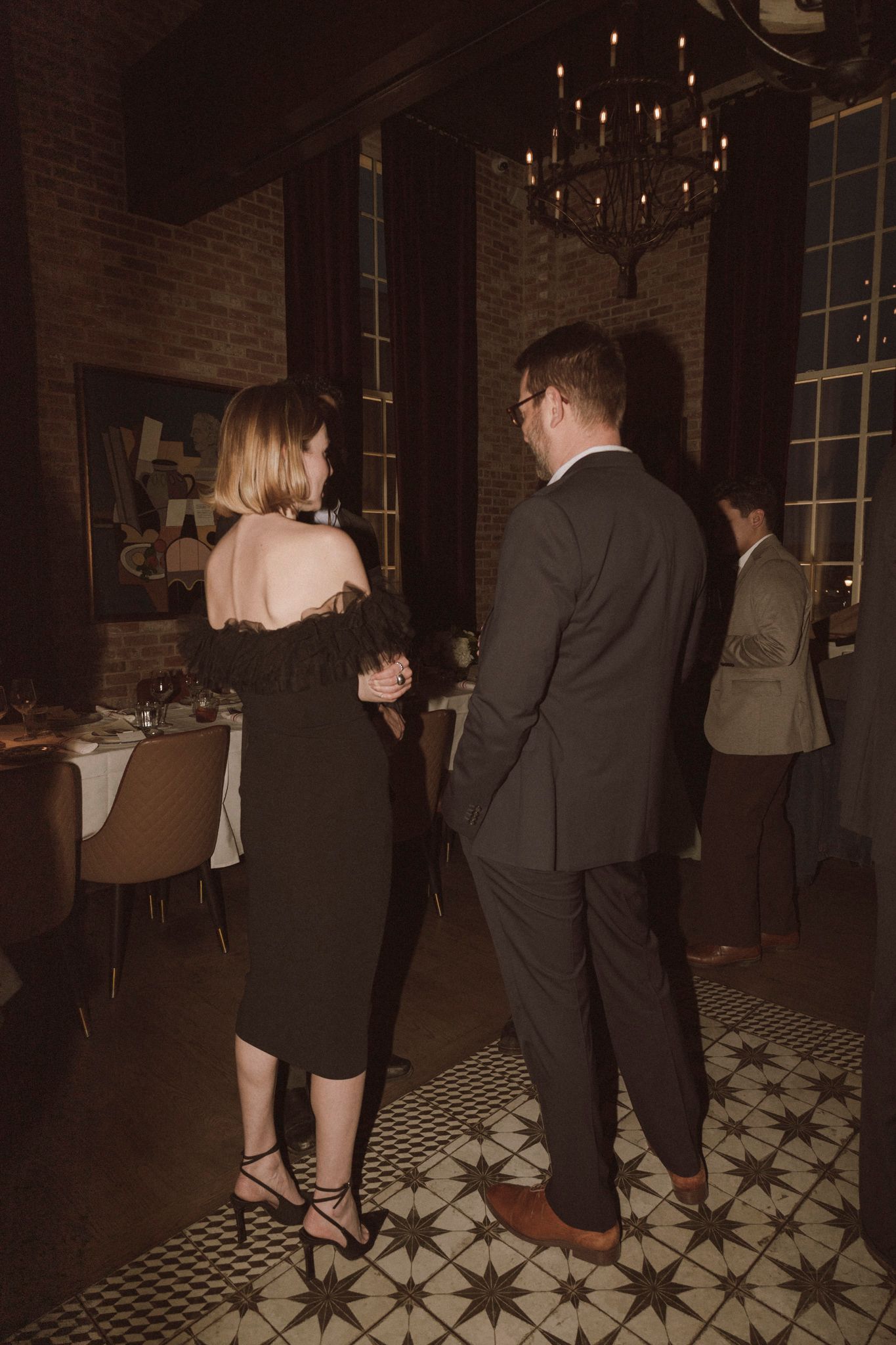 Guests in formal attire converse at an elegant dimly lit wedding reception venue with chandelier.