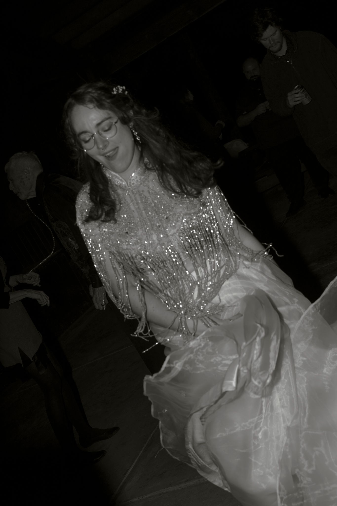 A performer in a sparkling white outfit dances gracefully in a dark setting during a stage performance.