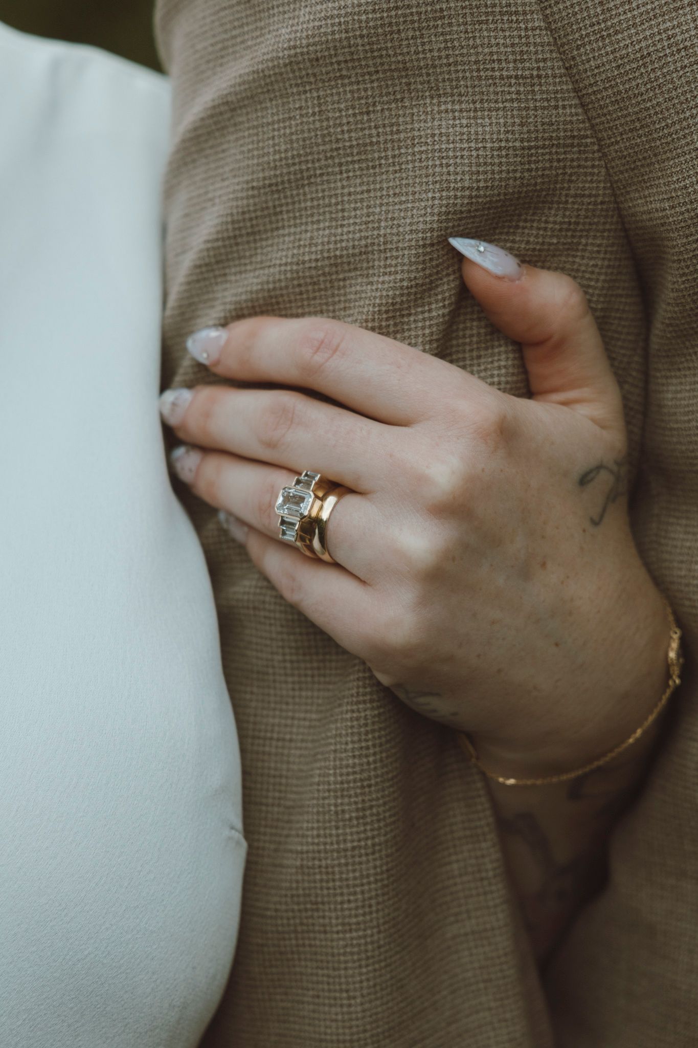 Close-up of hands showing off wedding rings against a textured fabric background.