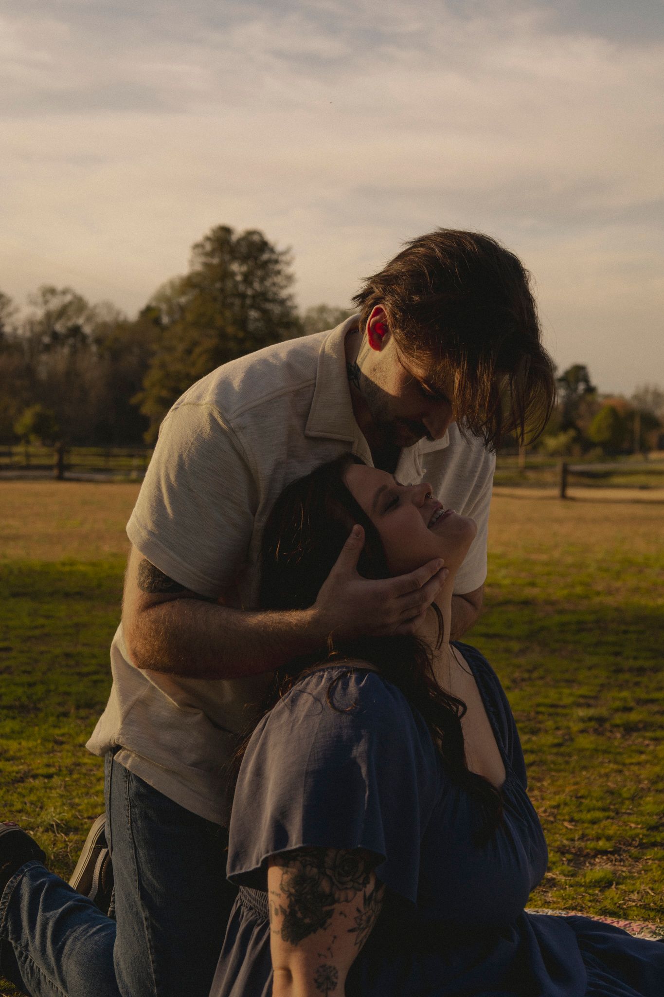 A couple shares an intimate moment in a park during golden hour with trees and grass in the background.