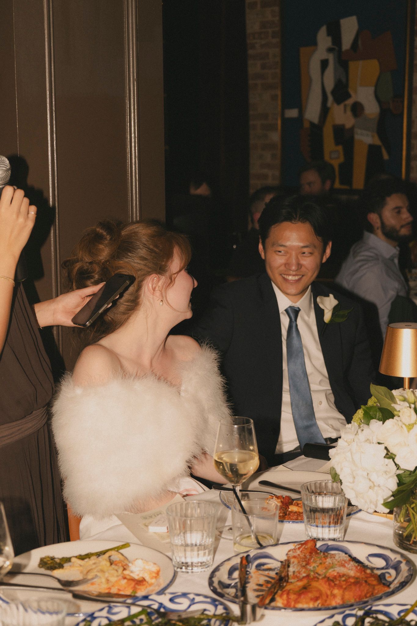 Bride and groom smiling together at their wedding reception table with white floral centerpiece and candles.