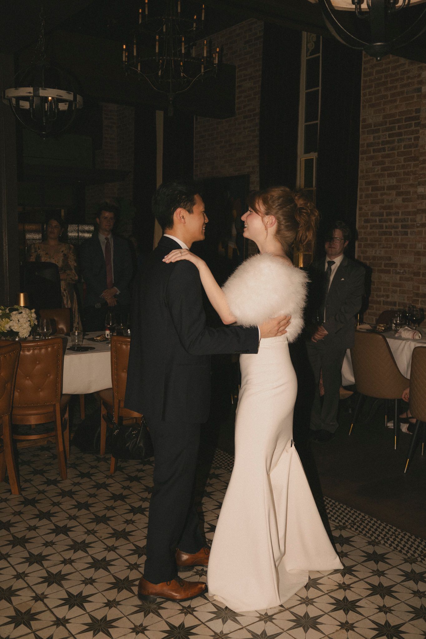Bride and groom sharing first dance in elegant venue with chandelier and patterned floor.