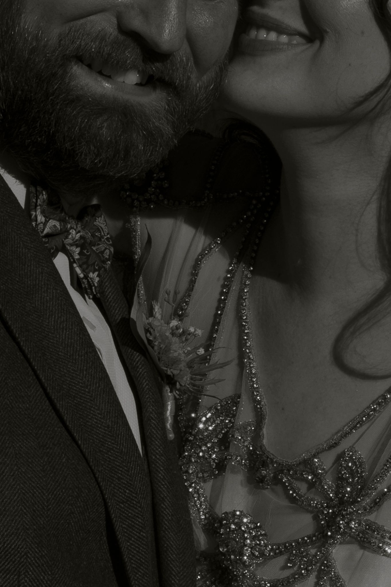 A black and white close-up photograph of a couple in formal attire with sparkly jewelry details.