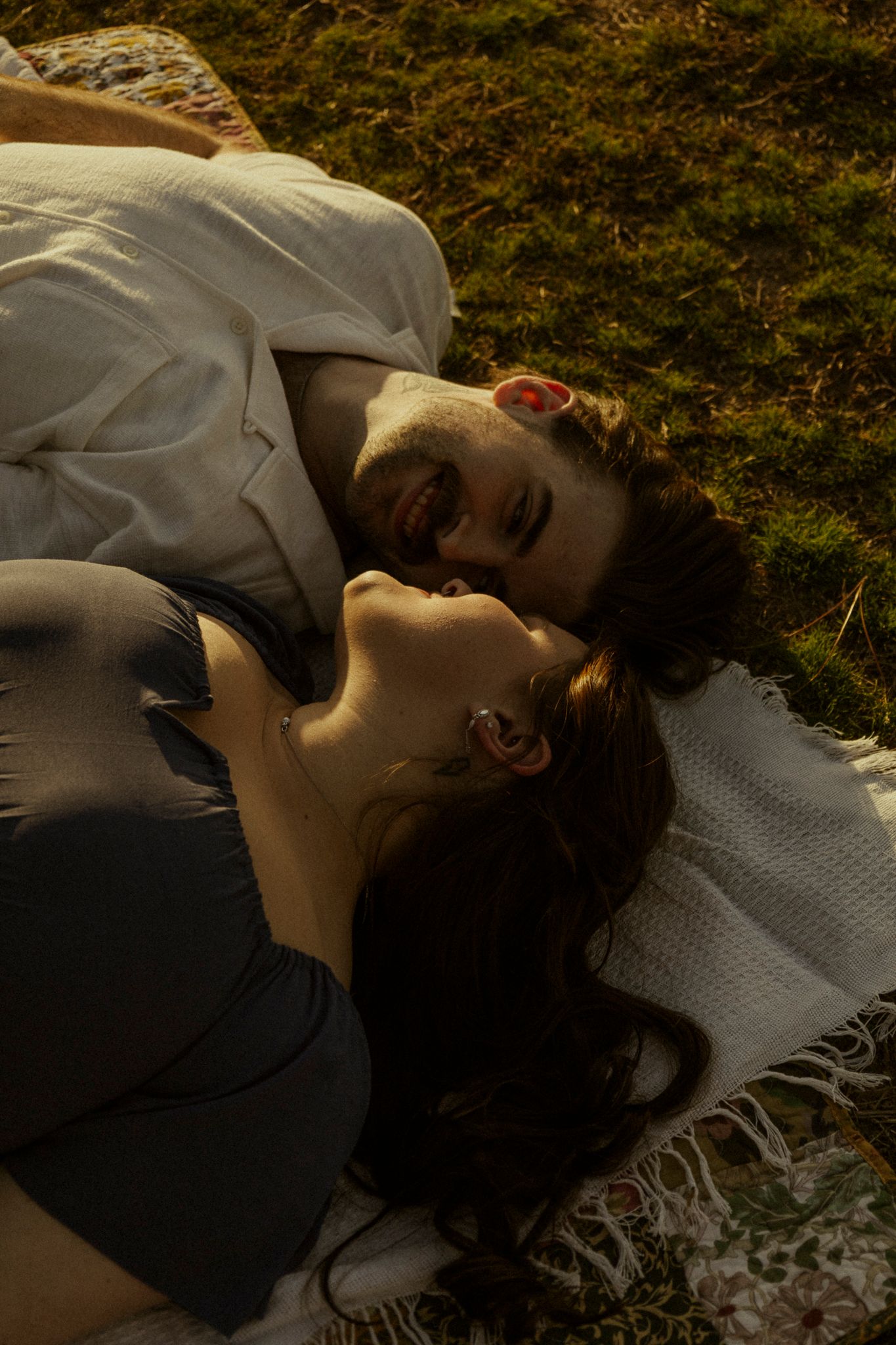 Romantic couple lying together on a blanket outdoors, smiling and enjoying a peaceful moment.