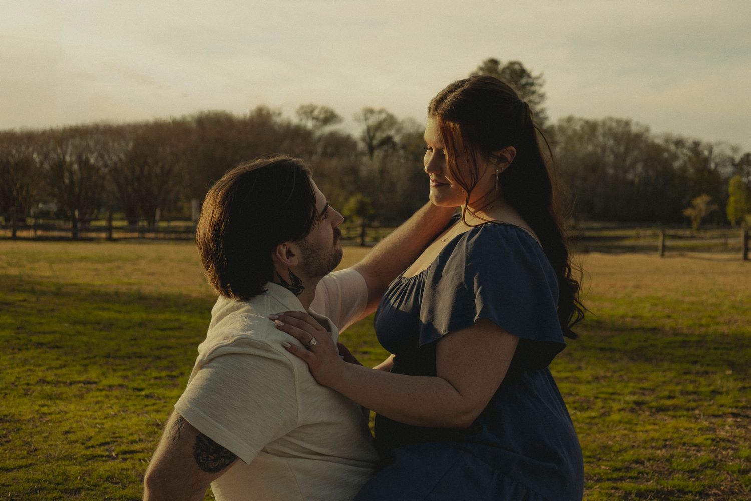 A couple shares a tender moment in a sunlit park, the woman gently touching the man's face.