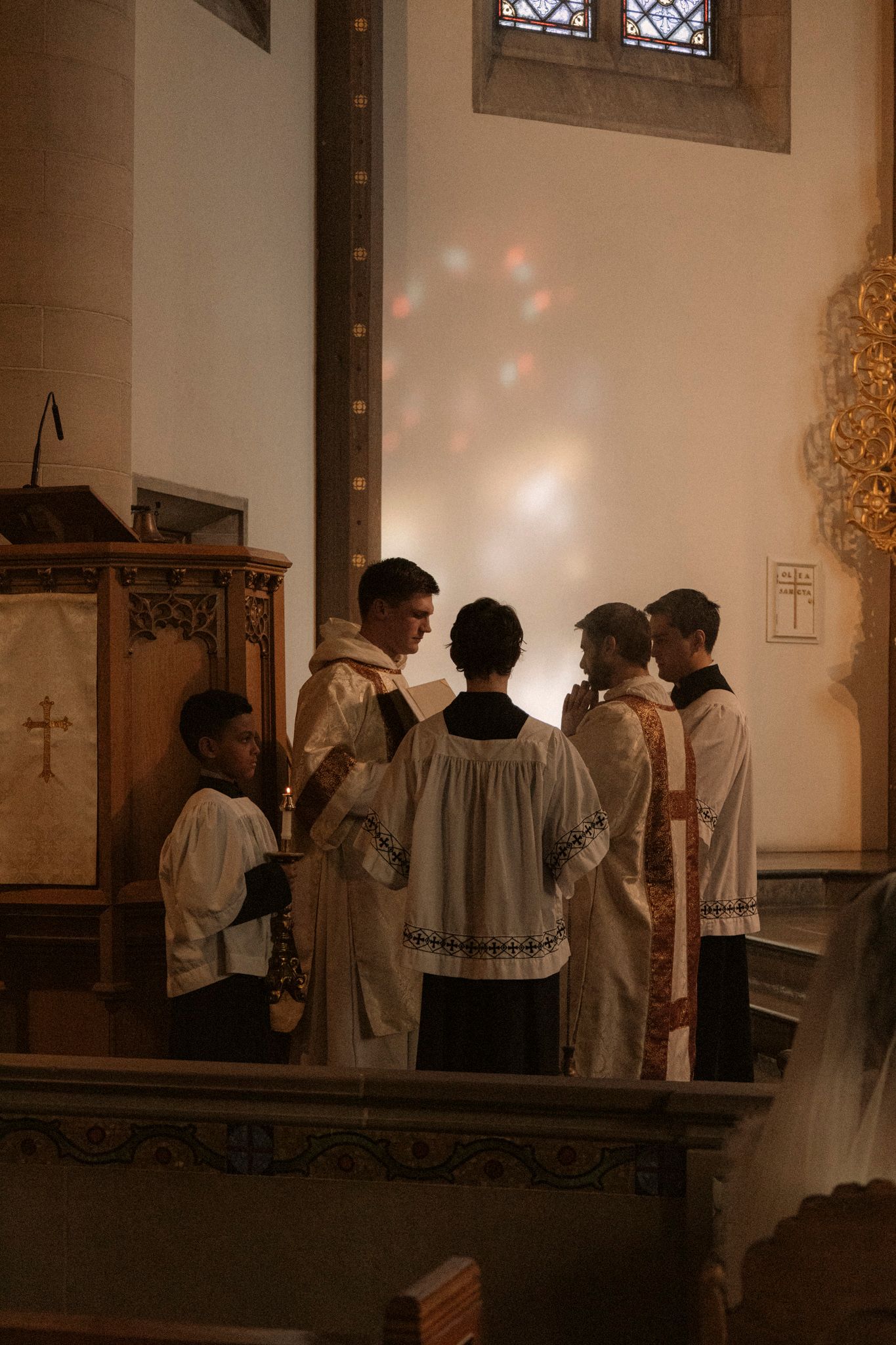 Altar servers and clergy in white robes gathered near the church altar during a wedding ceremony.