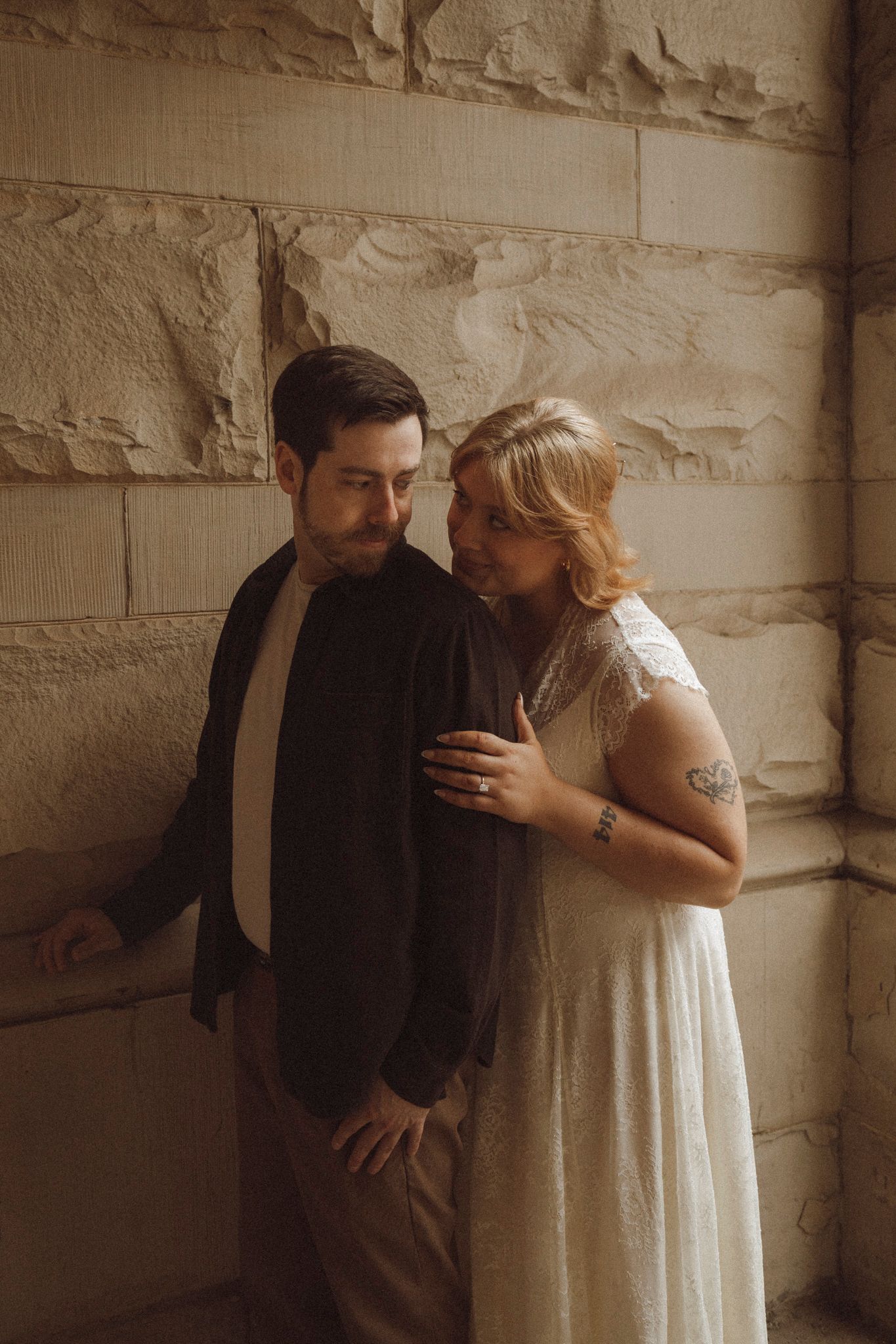 A couple in wedding attire shares an intimate moment against a stone wall in a series of romantic sepia-toned photos.