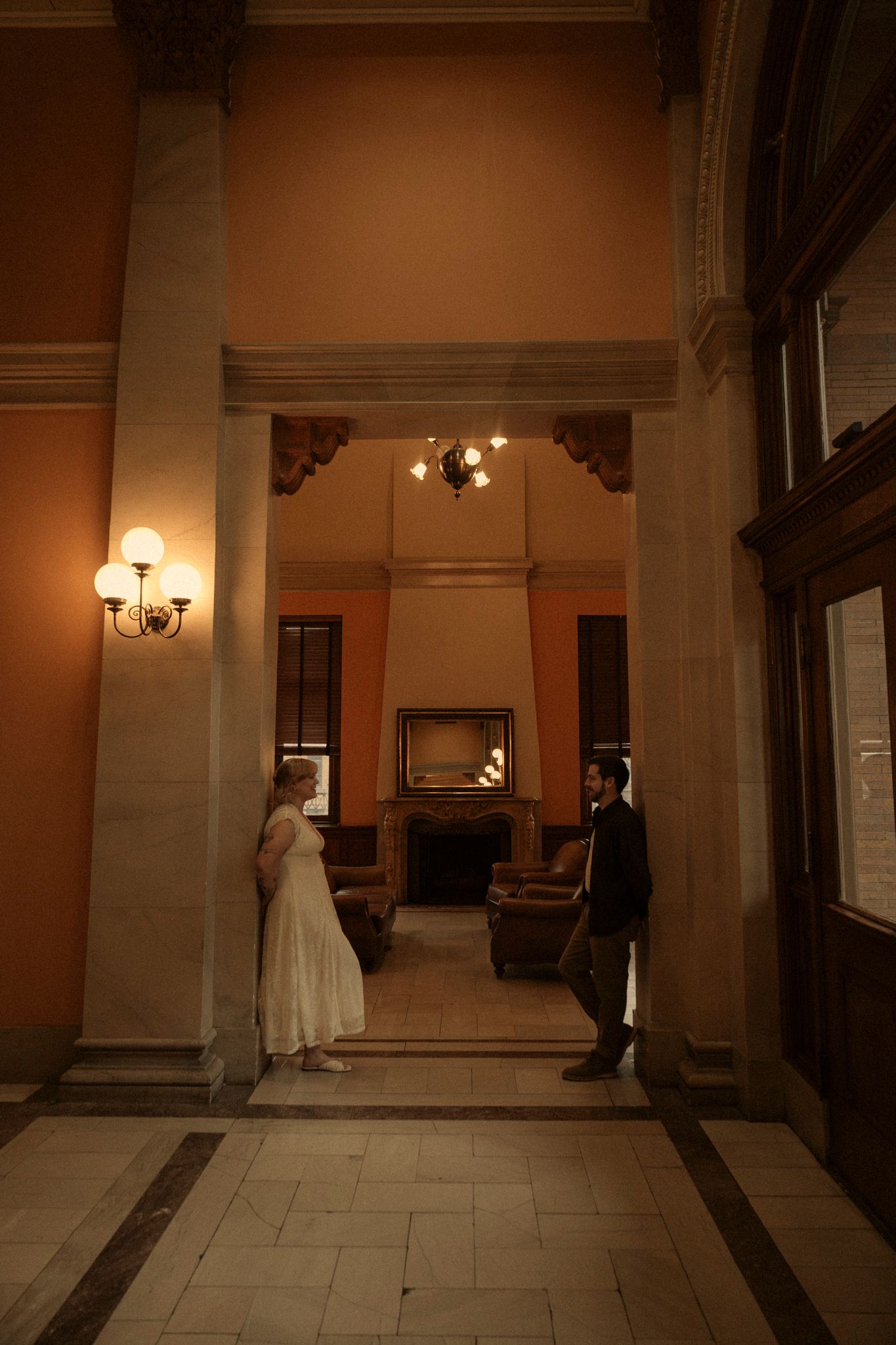 A dimly lit hallway with classical architectural details and wall sconces creates a moody, atmospheric interior scene.