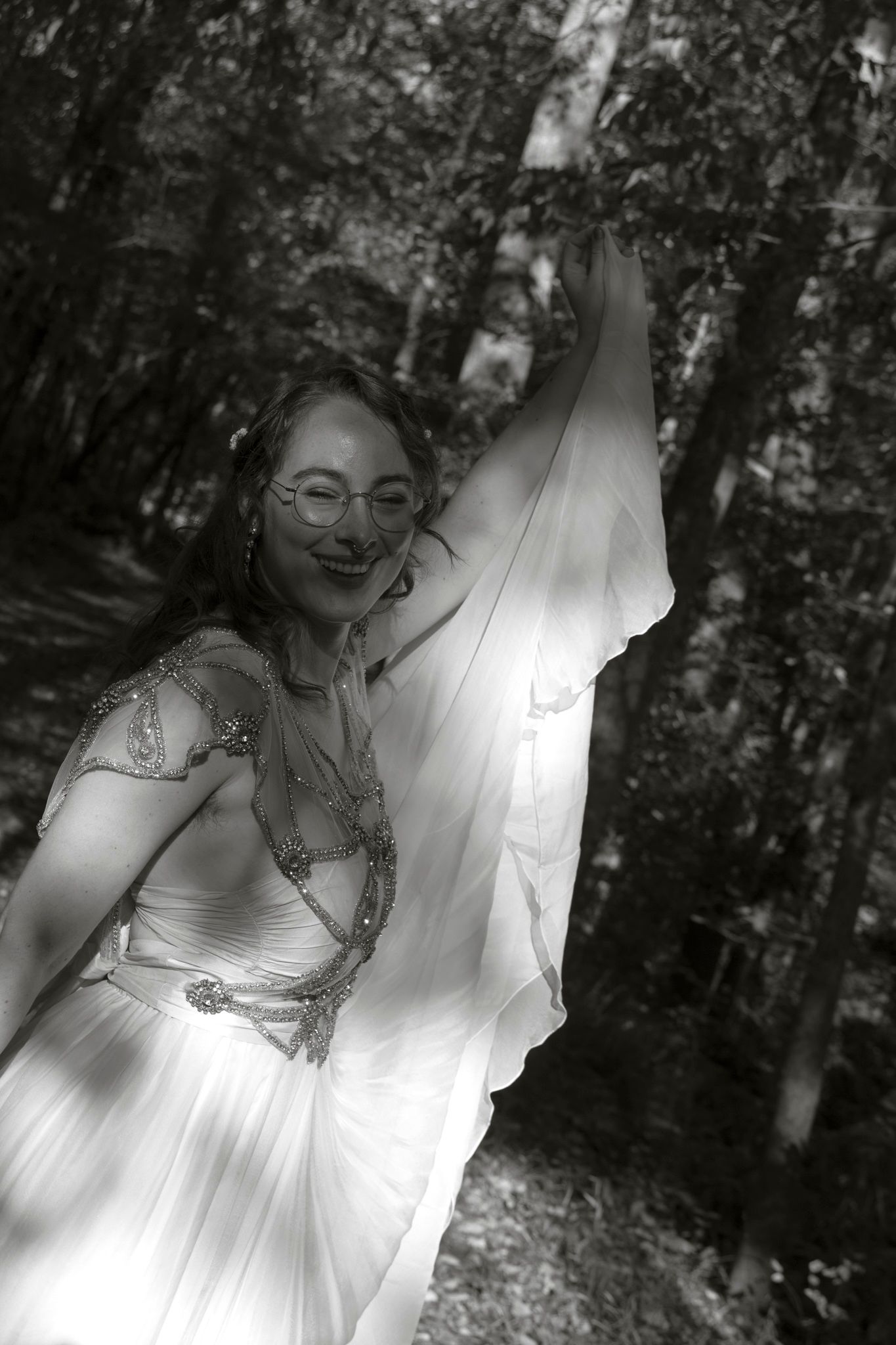 A black and white photo shows a dreamy forest scene with a flowing white dress and dappled sunlight.
