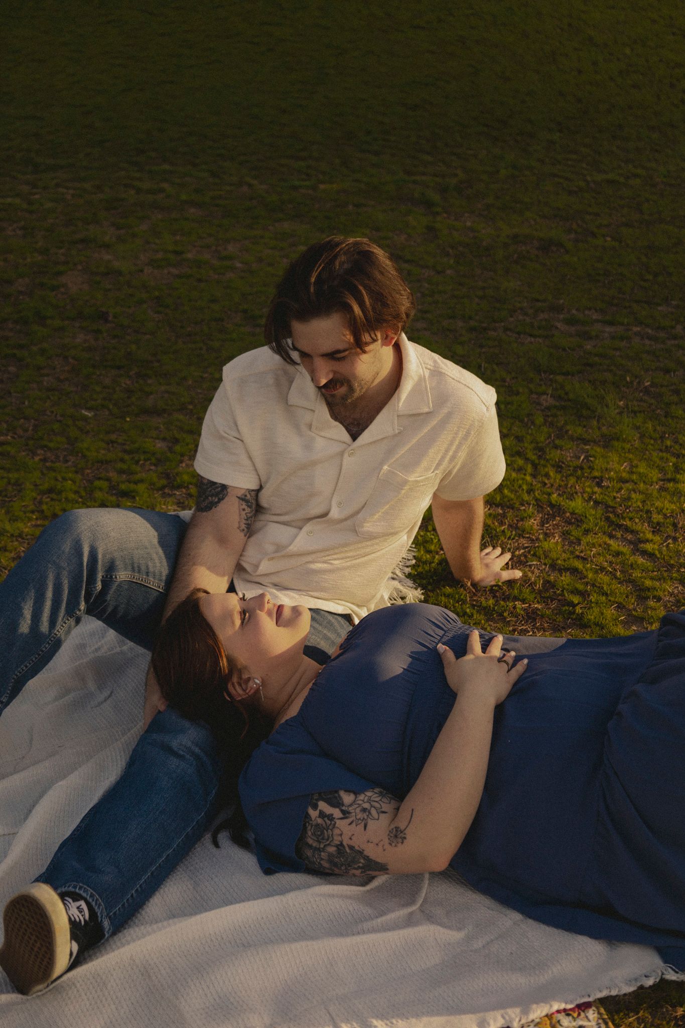 A couple lies together on a blanket outdoors sharing an intimate moment at dusk.