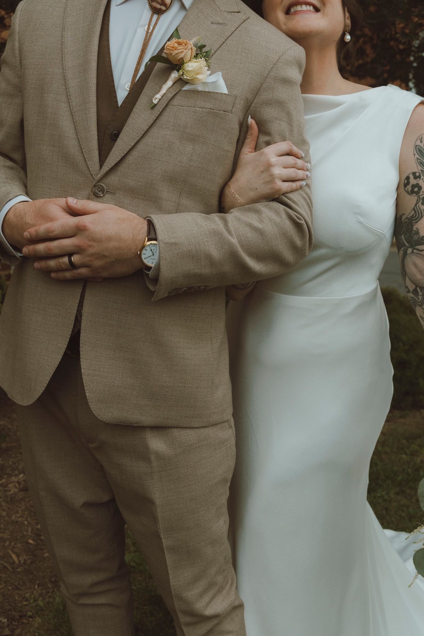 A couple in wedding attire, with the groom in a tan suit and bride in a white dress, embrace during their photoshoot.