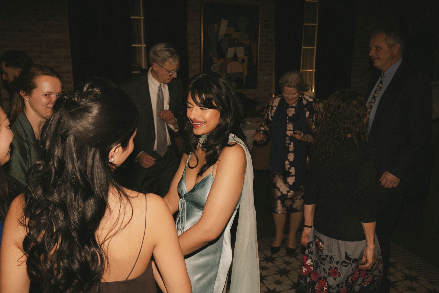 Wedding guests in elegant attire mingle and socialize during a dimly lit reception celebration.