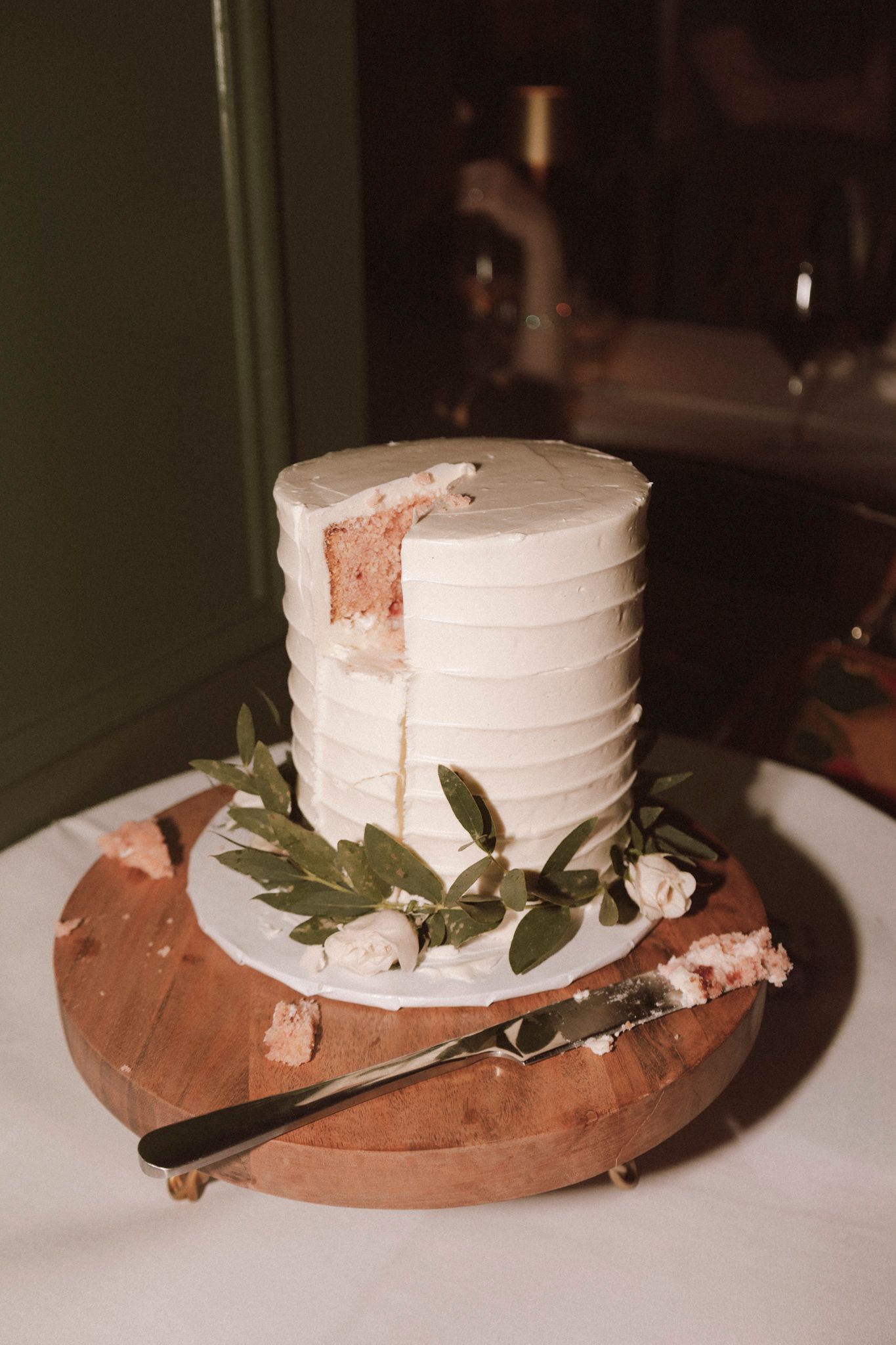 Elegant single-tier white wedding cake with greenery and roses on wooden stand.