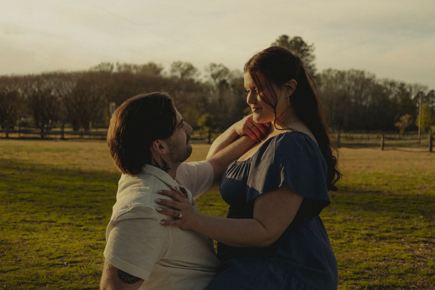 Romantic couple embracing in a golden sunset field, sharing a tender moment outdoors.