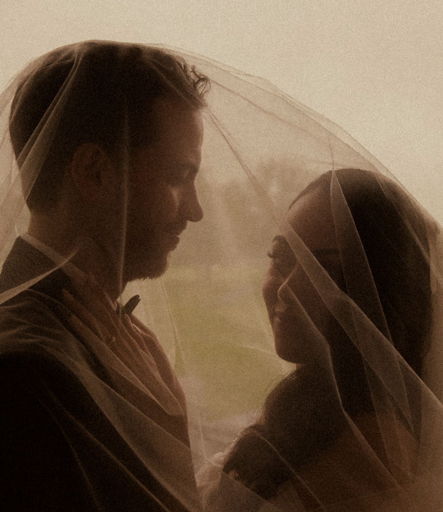 Romantic couple sharing an intimate moment under a sheer bridal veil in soft, warm-toned wedding photography.