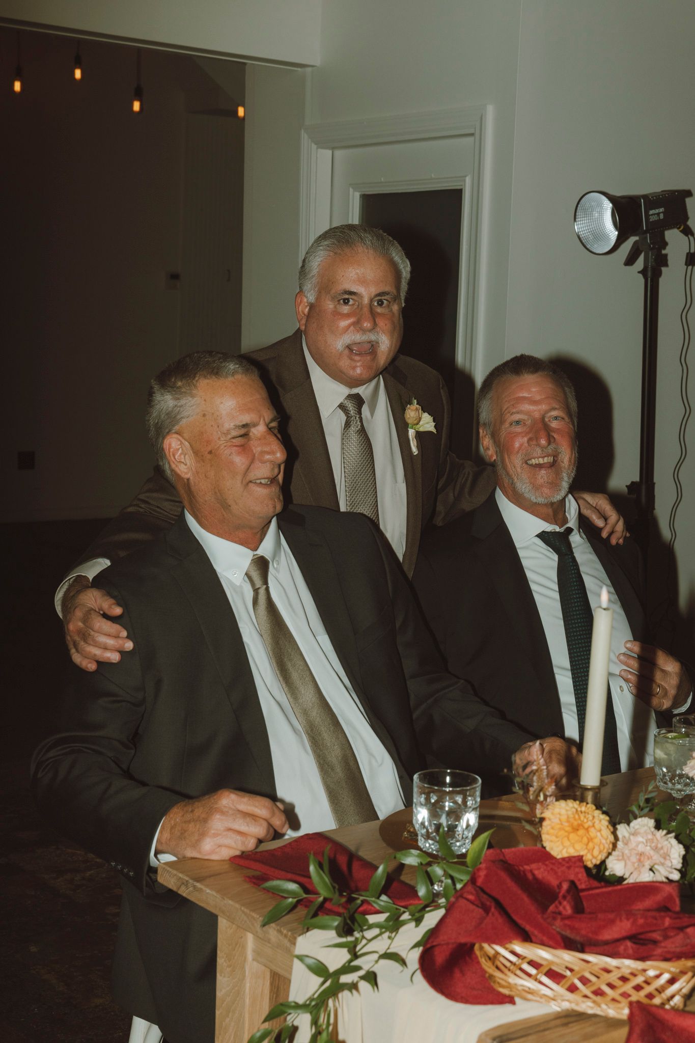 Two guests in formal attire share a laugh while seated at an elegantly decorated dinner table with red tablecloth.