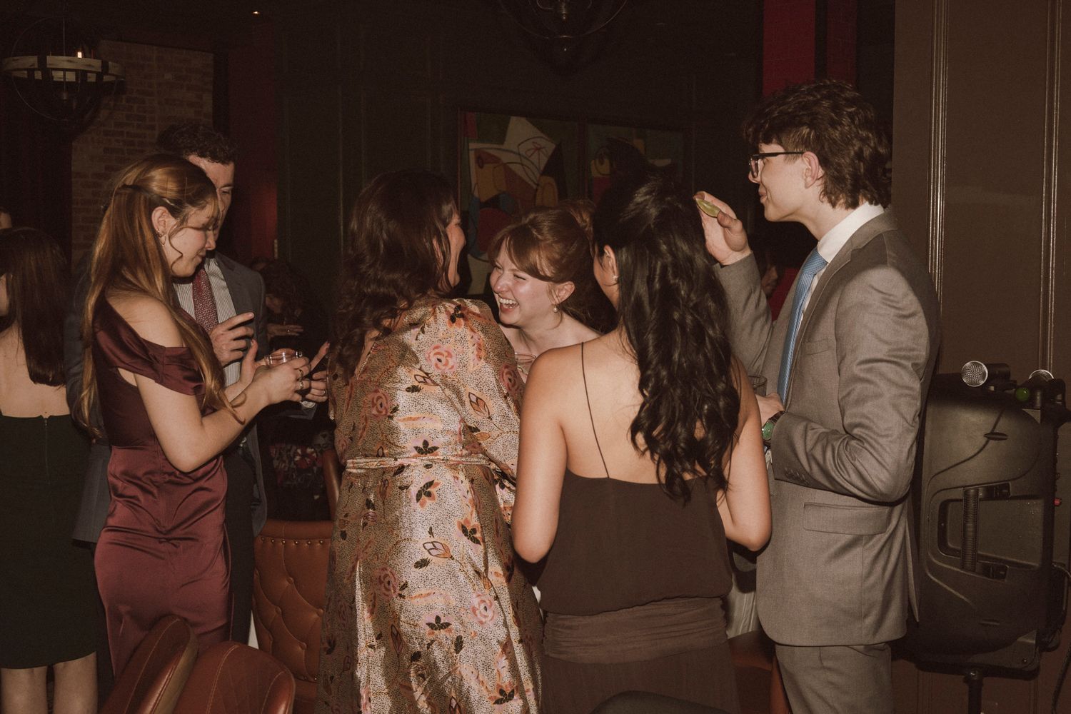 Young wedding guests in formal attire socialize and laugh together on the dance floor at reception.