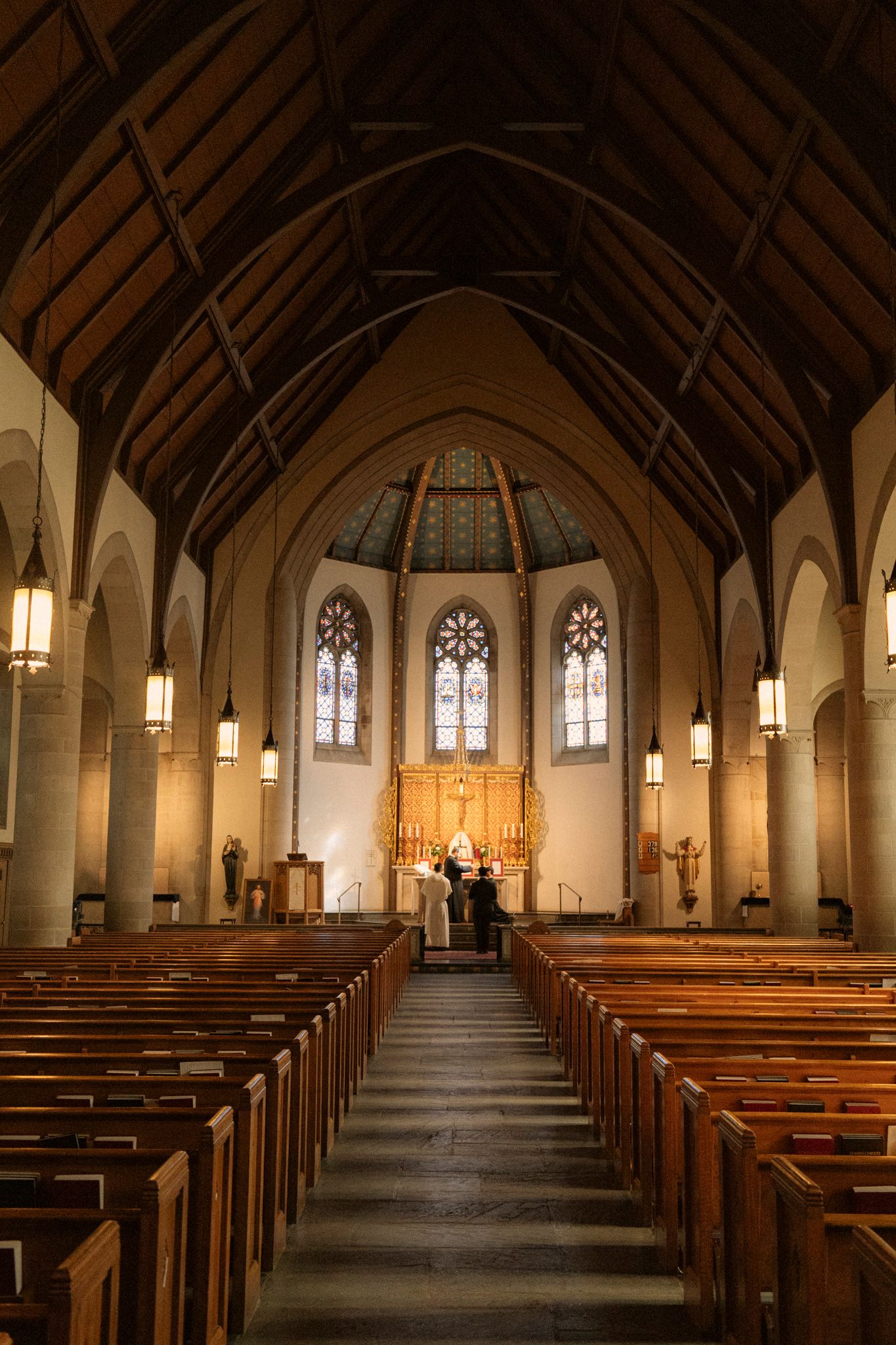 Church nave interior with wooden pews leading to ornate golden altar and stained glass windows.