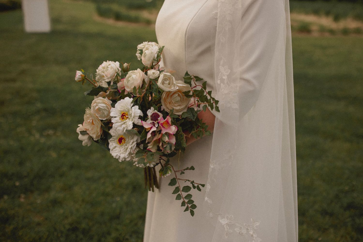 A close-up view of a white wedding dress with a delicate floral bouquet featuring roses and daisies in soft colors.