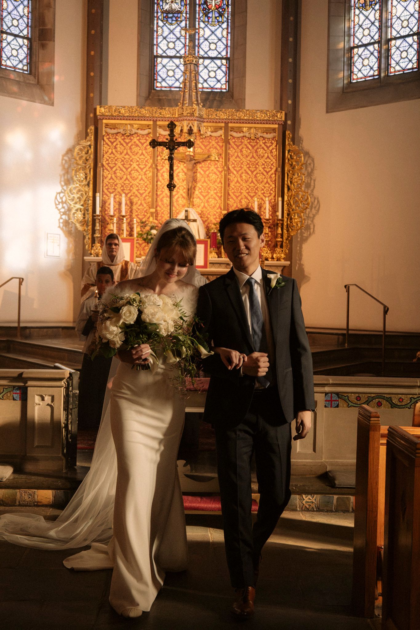 Bride and groom walk down church aisle after wedding ceremony at ornate altar.