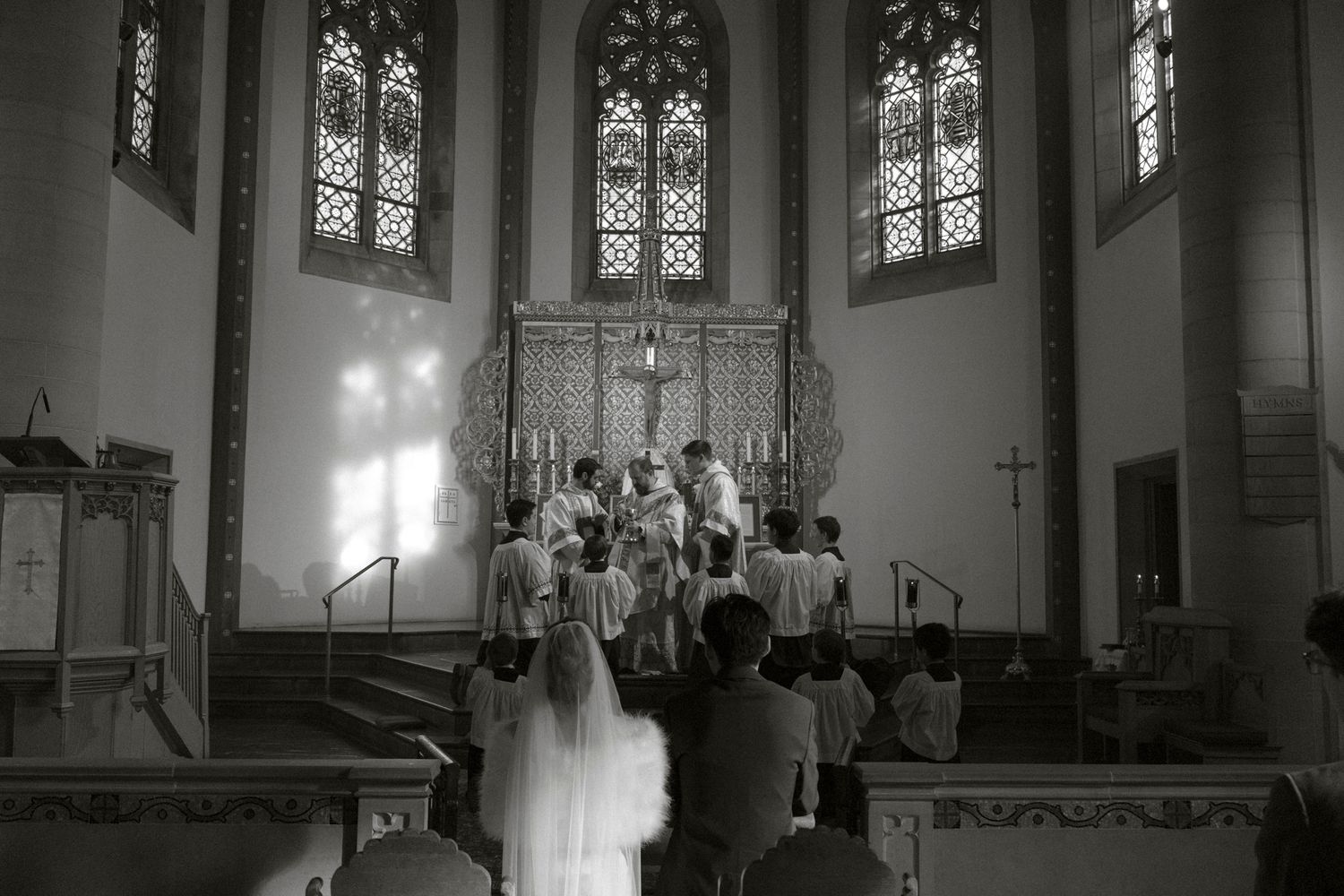 Black and white photo of a church choir performing at the altar during a religious ceremony with stained glass windows.