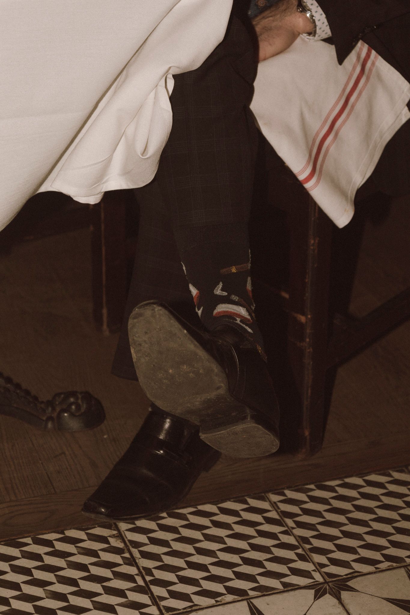 Close-up of a waiter's feet on black and white tiled floor, wearing dress shoes with colorful socks at a wedding reception.