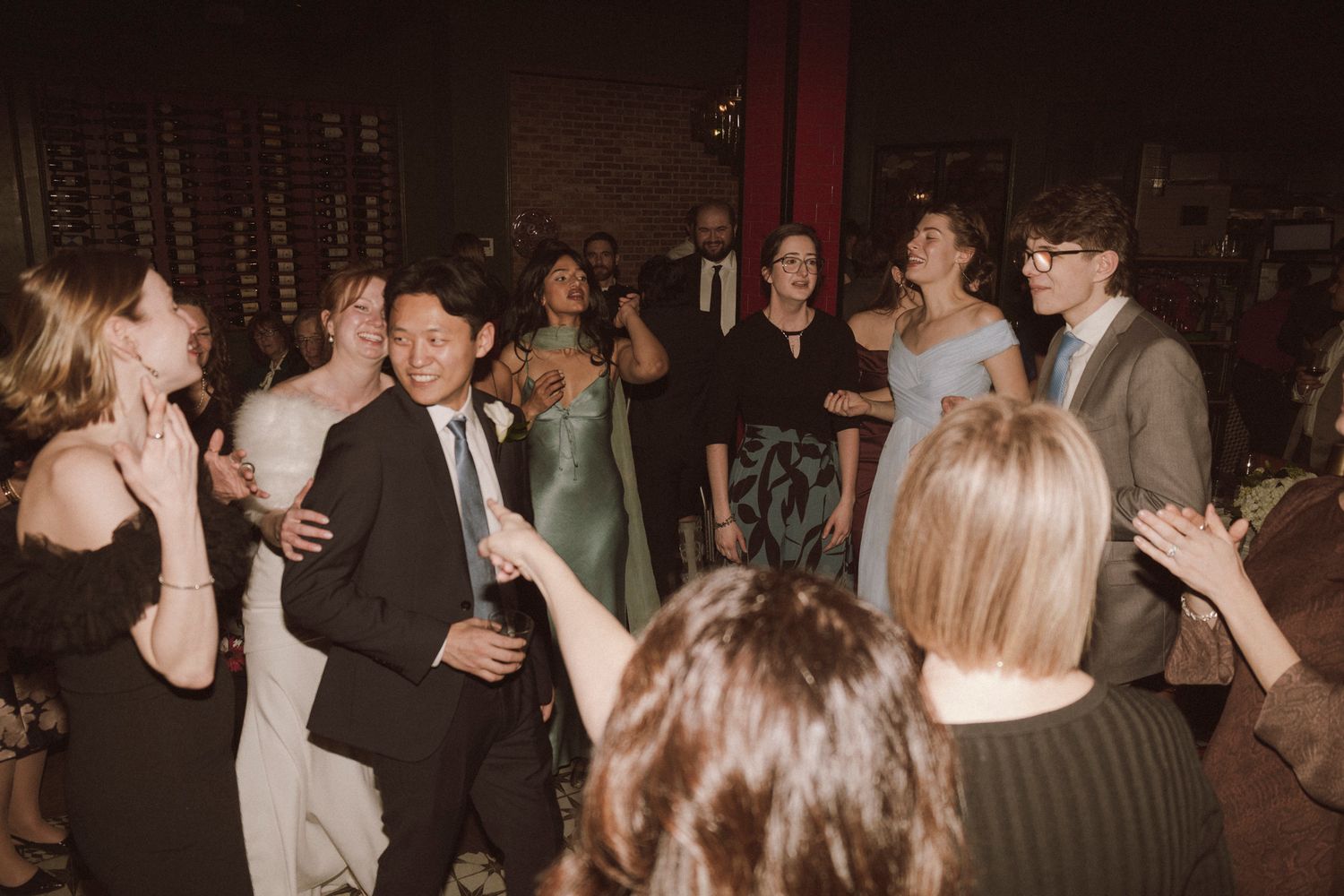 Guests celebrating and dancing together at a lively wedding reception in a warmly lit venue.