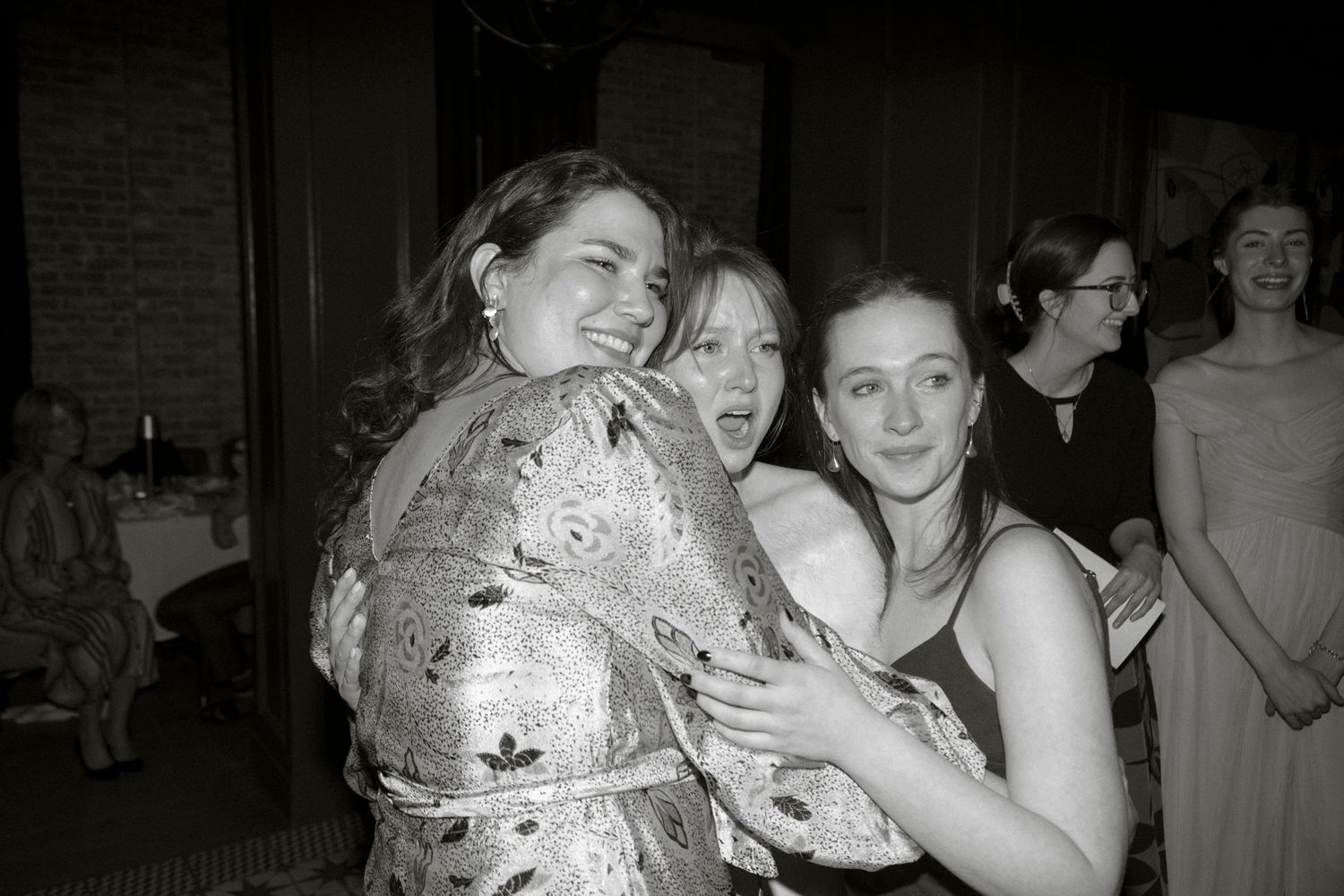 Three women laughing and embracing at wedding reception in black and white photo.