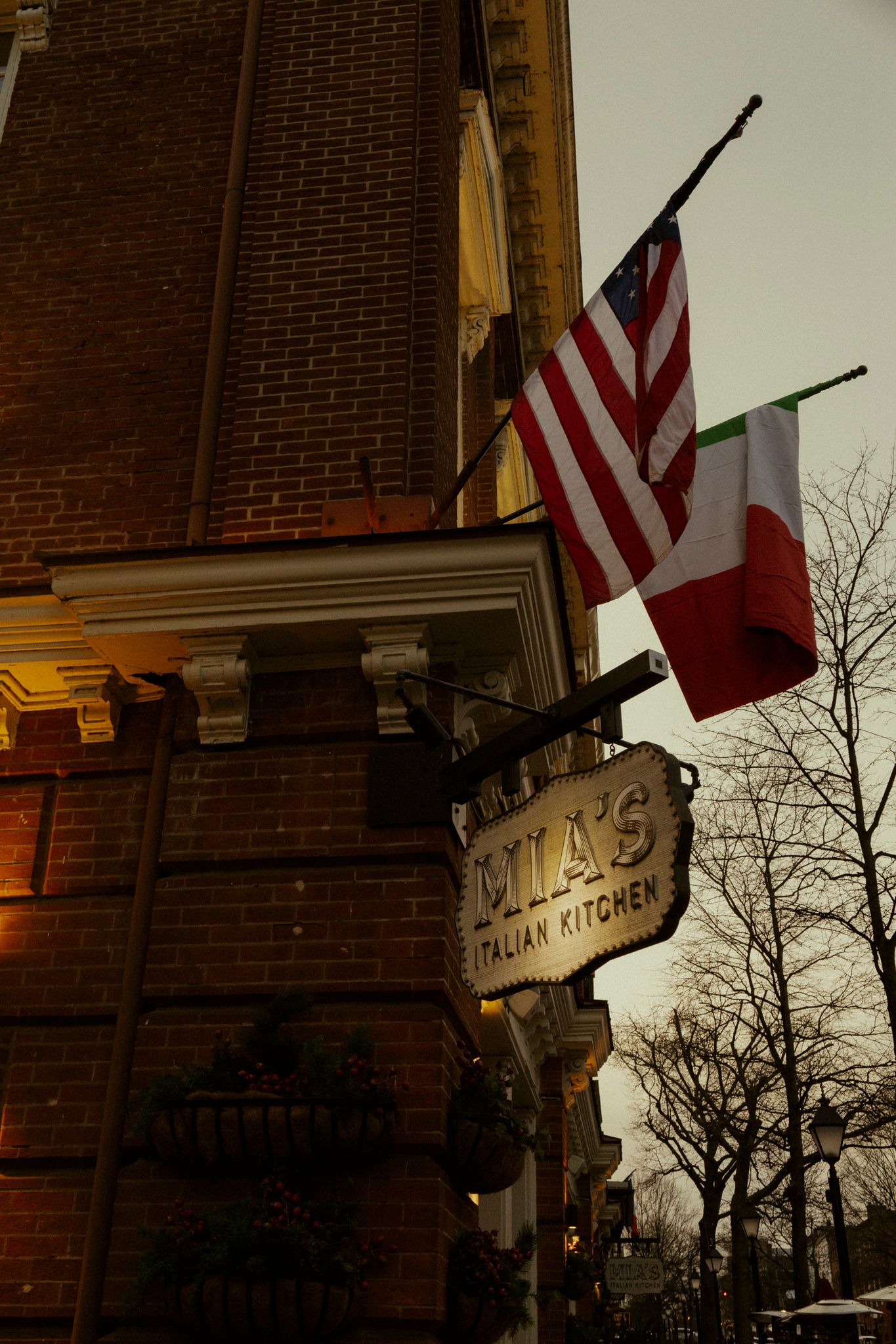 Mia's Italian Kitchen restaurant exterior with American and Italian flags on a brick building at dusk.