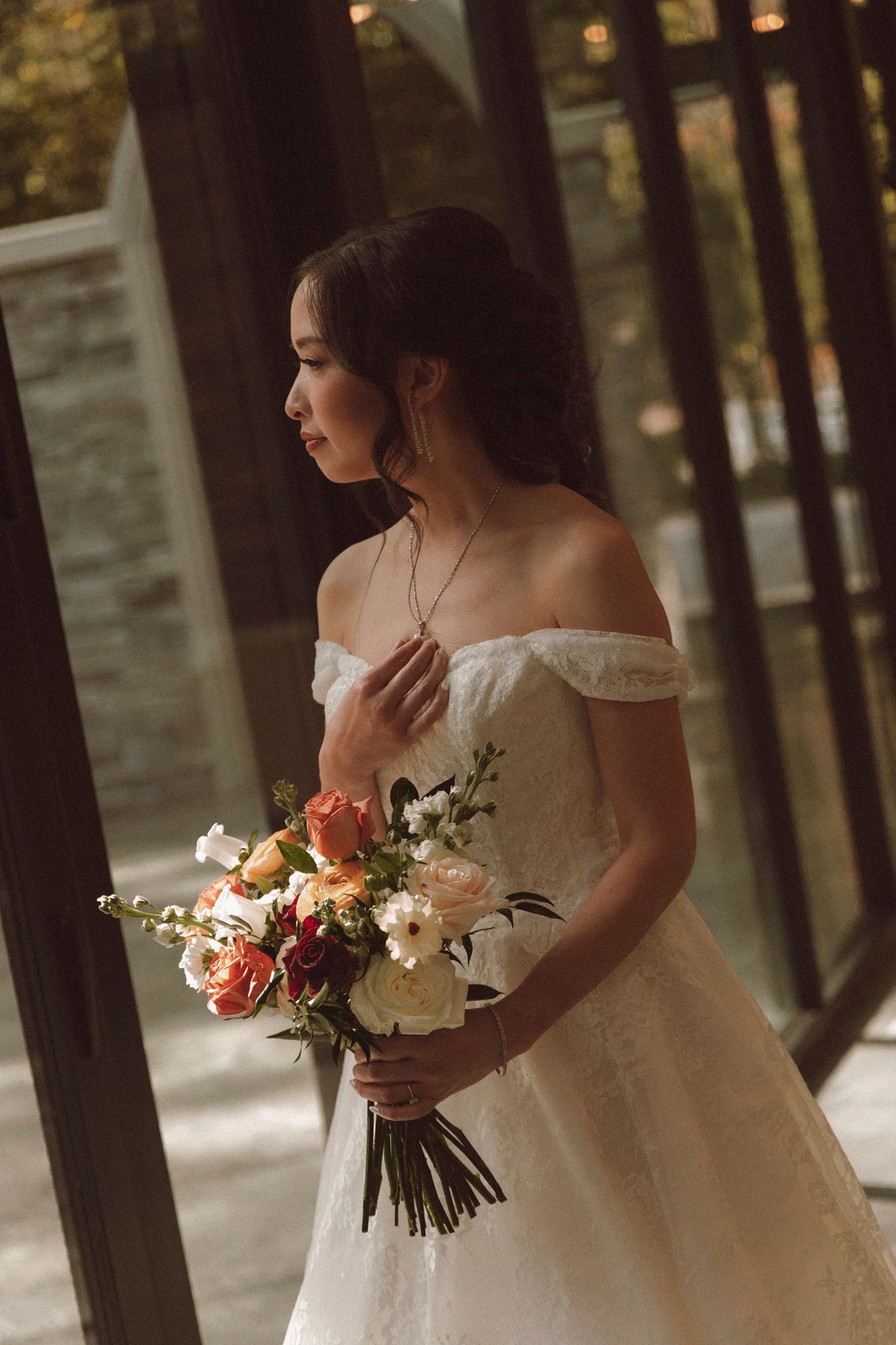 A bride in a white wedding gown holds a colorful bouquet of roses and flowers in a forest setting.