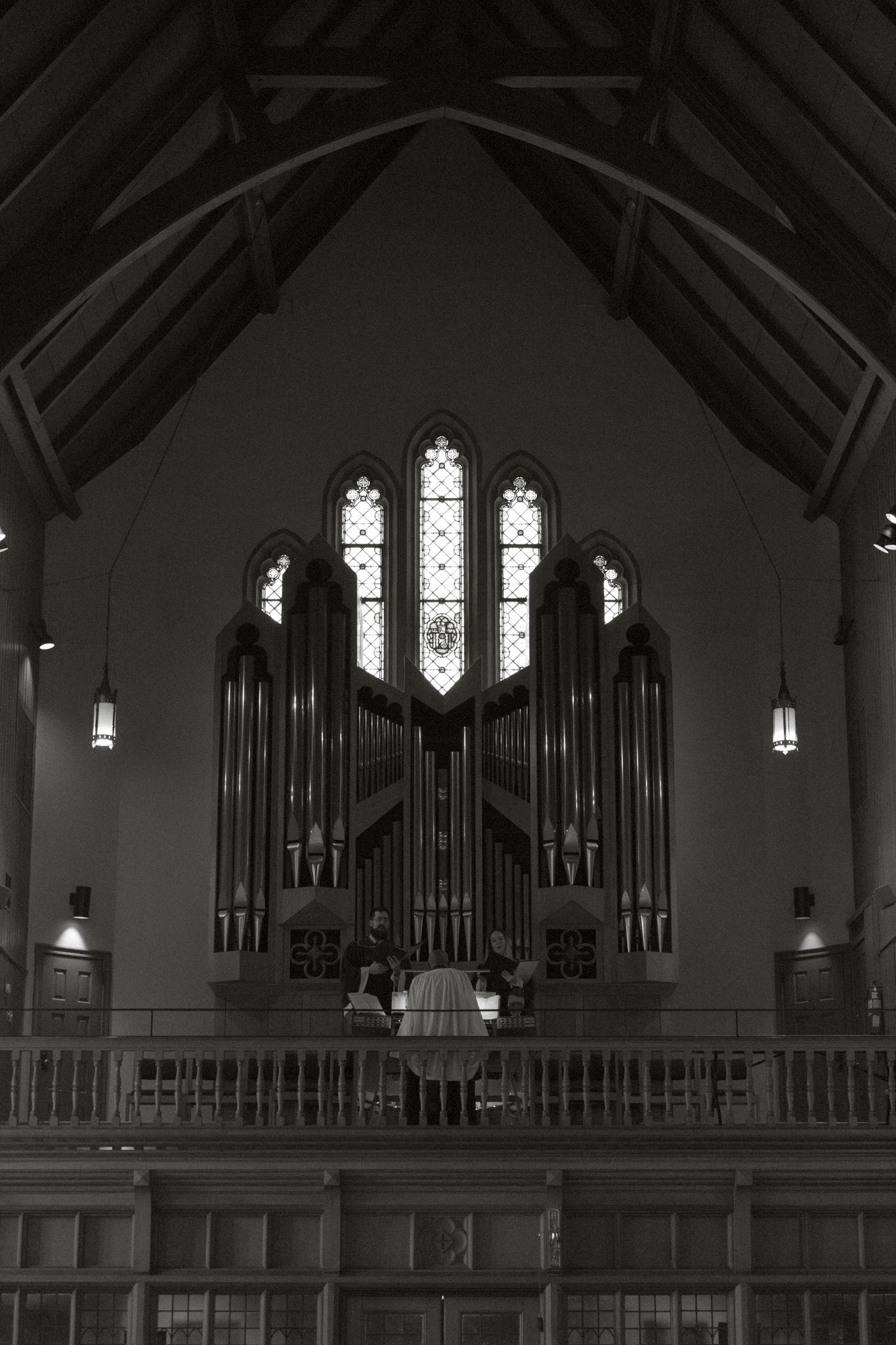 Black and white photo of church organ pipes beneath Gothic stained glass windows.
