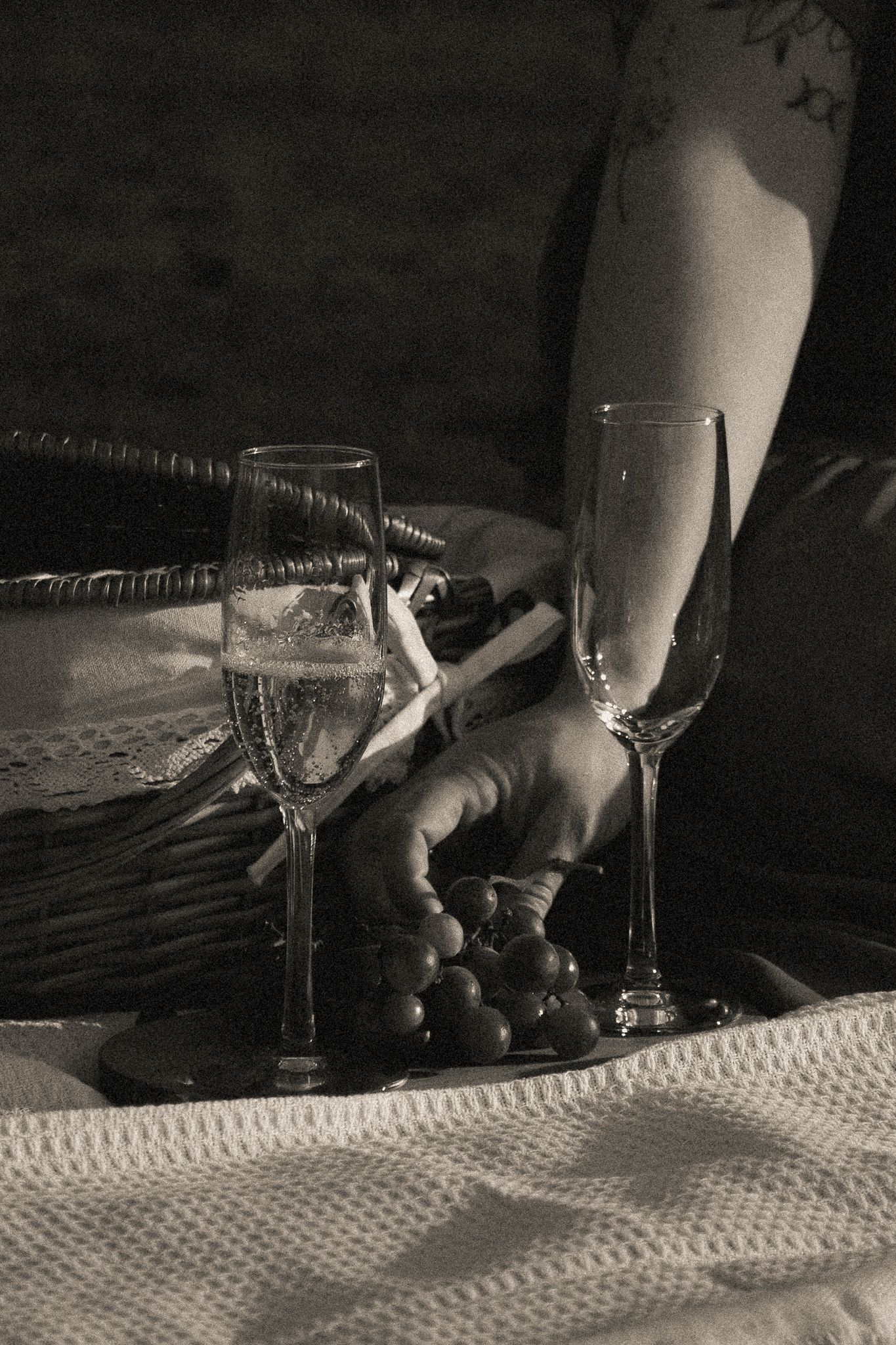 Black and white photo of champagne flutes and grapes on a tray during a romantic picnic.