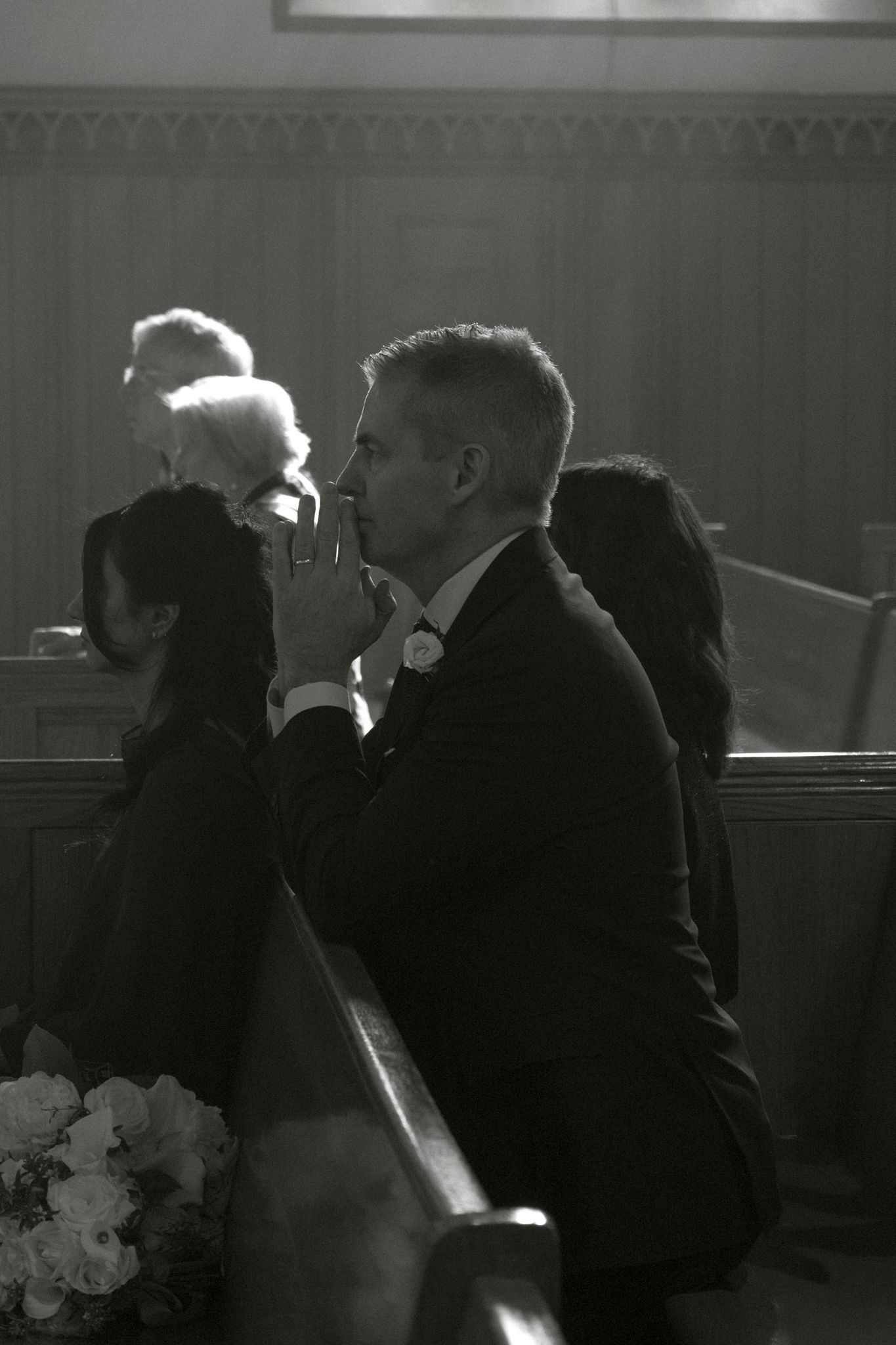 Black and white photo of a man in a suit sitting in church pews during a wedding ceremony.