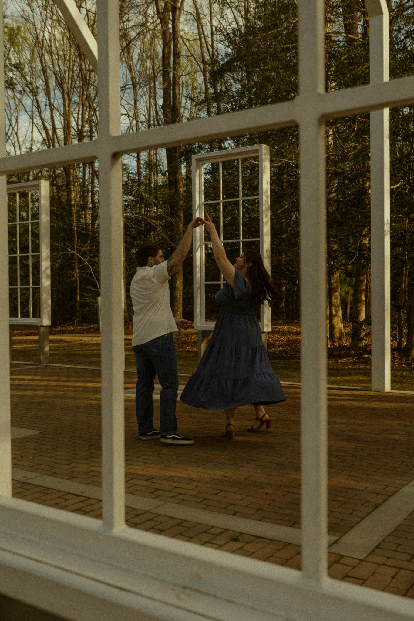 Couple dancing together in an outdoor garden pavilion surrounded by white window frames and autumn trees.