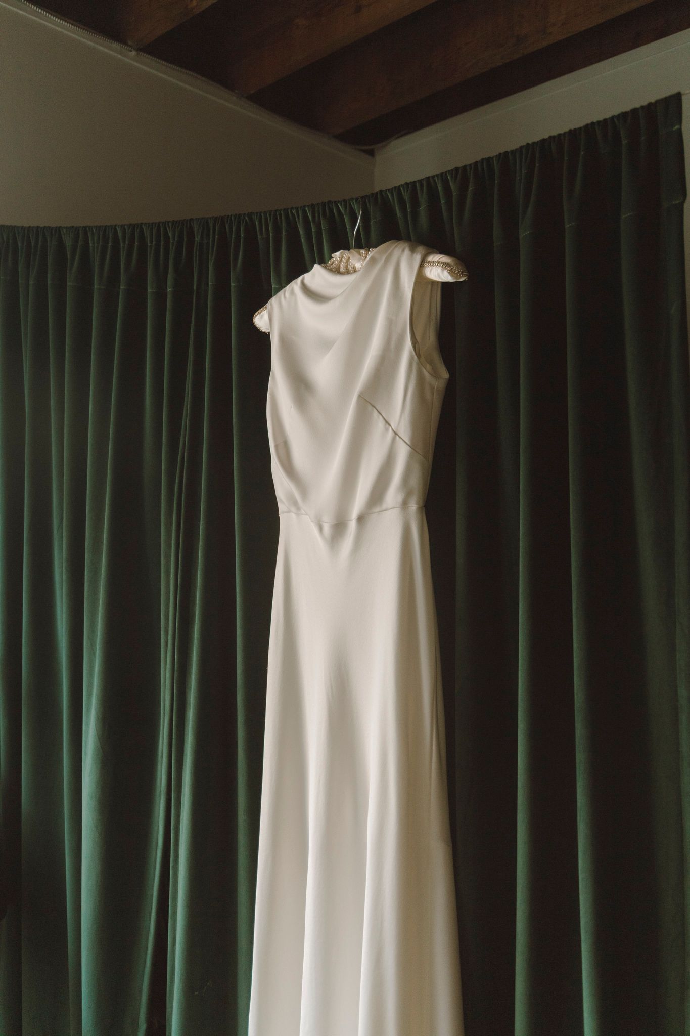 Four elegant white wedding dresses hanging on display against a dark green curtain backdrop.