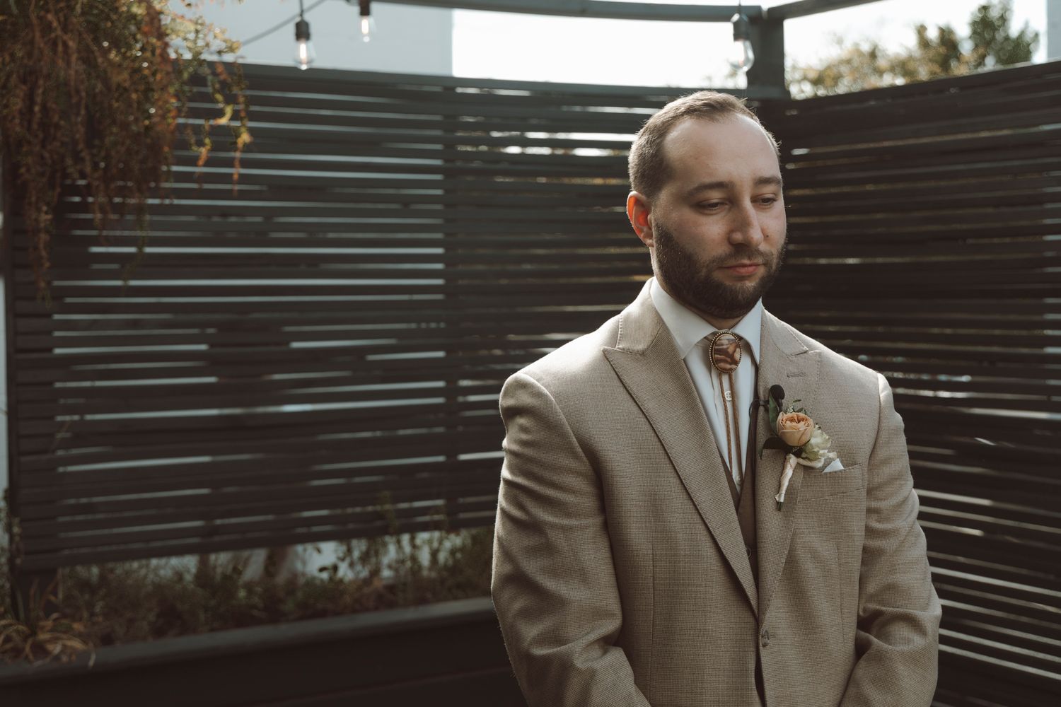 Couple in wedding attire stands together at outdoor venue with wooden slat backdrop during sunset ceremony.
