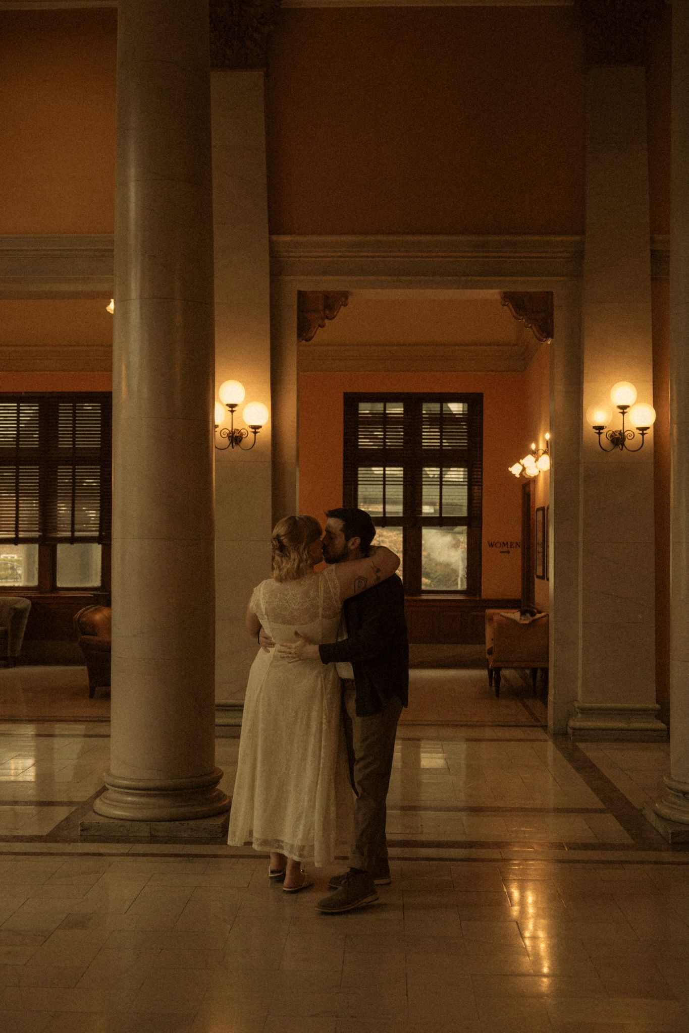 A romantic sequence of figures dancing in a dimly lit grand hallway with columns and warm lighting.