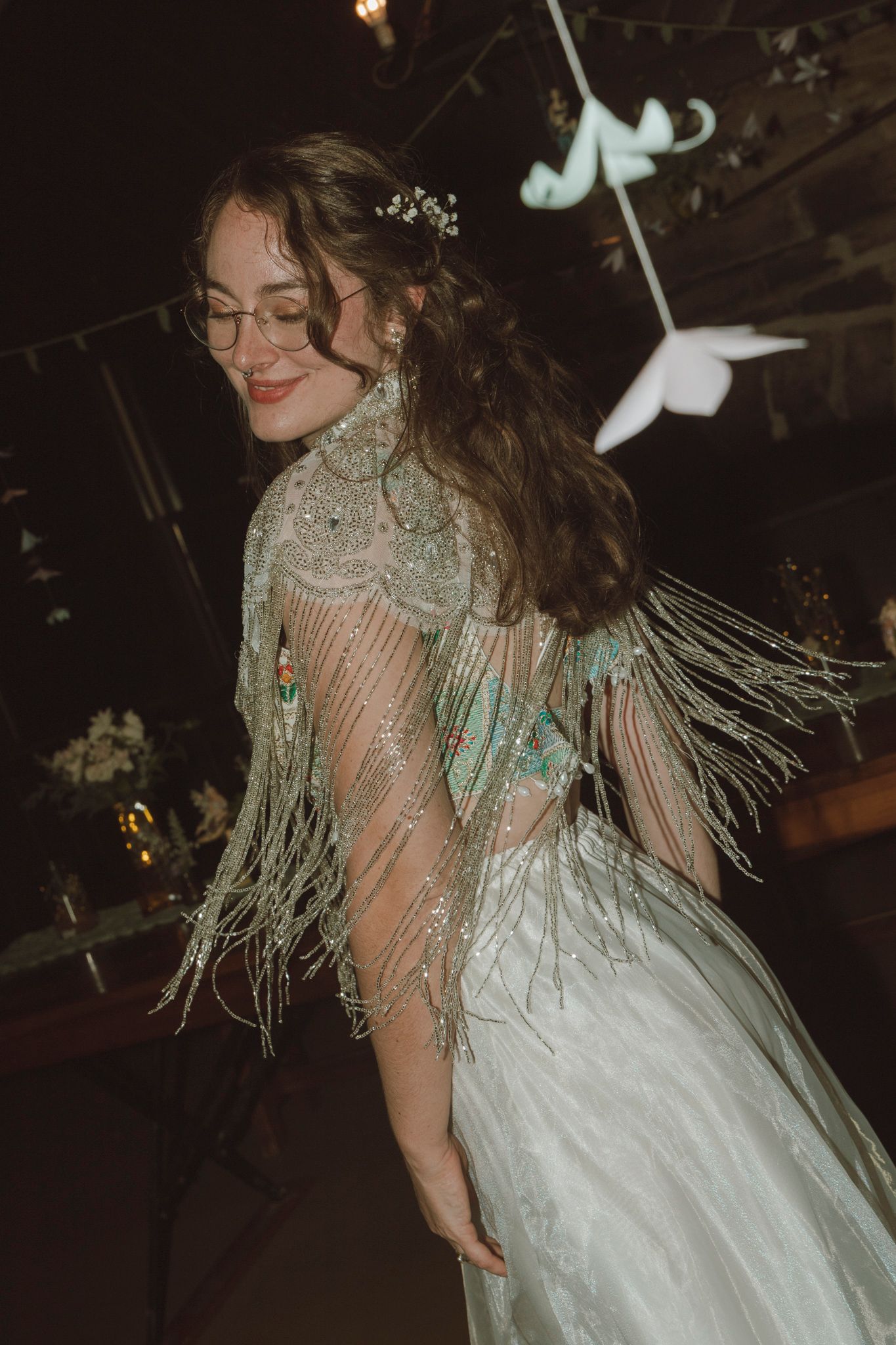 A person in a sparkly silver and white dress with fringe details twirls and dances in a dimly lit setting.