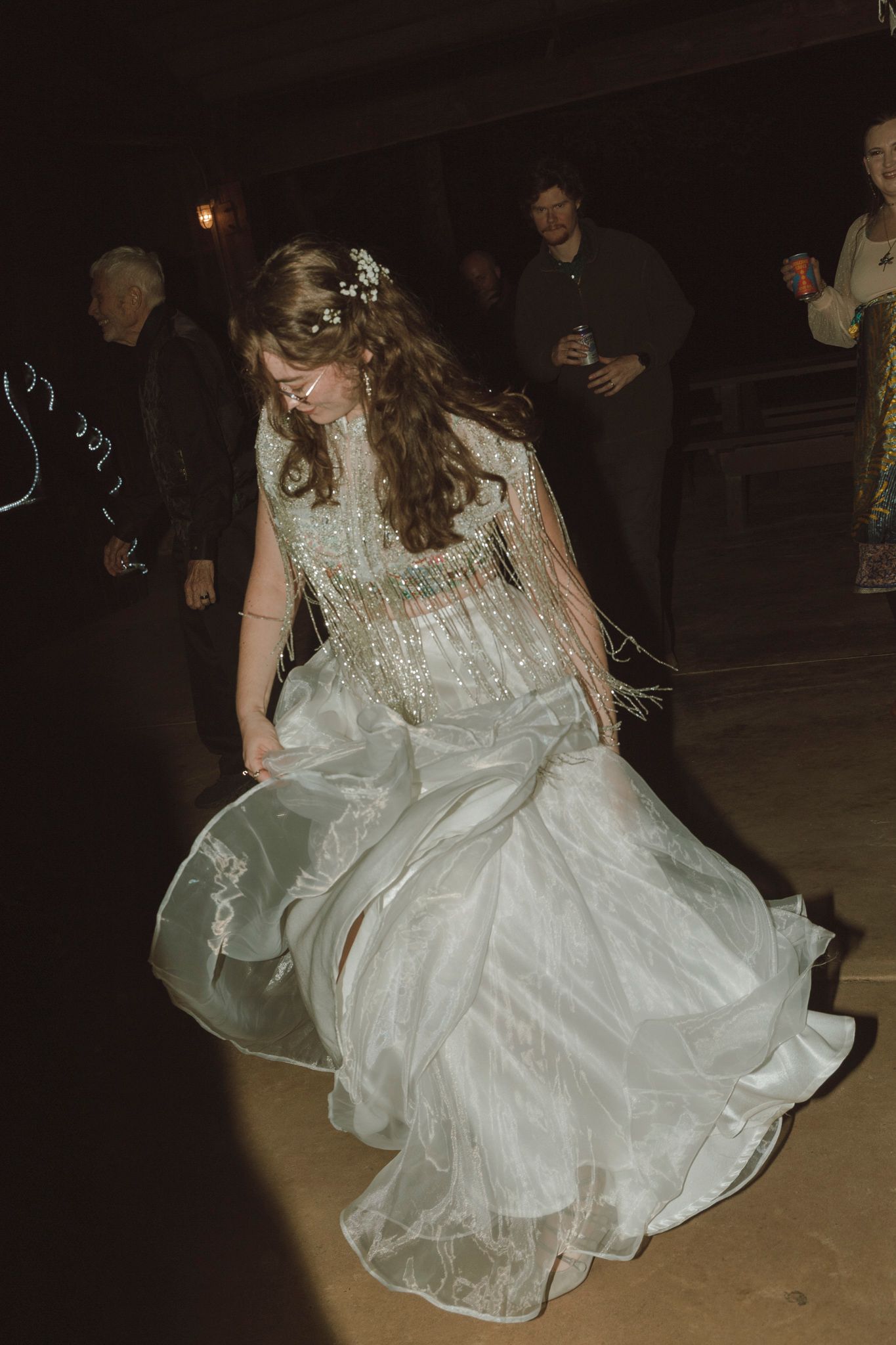 A person in a flowing white wedding dress dances at a dimly lit reception venue.