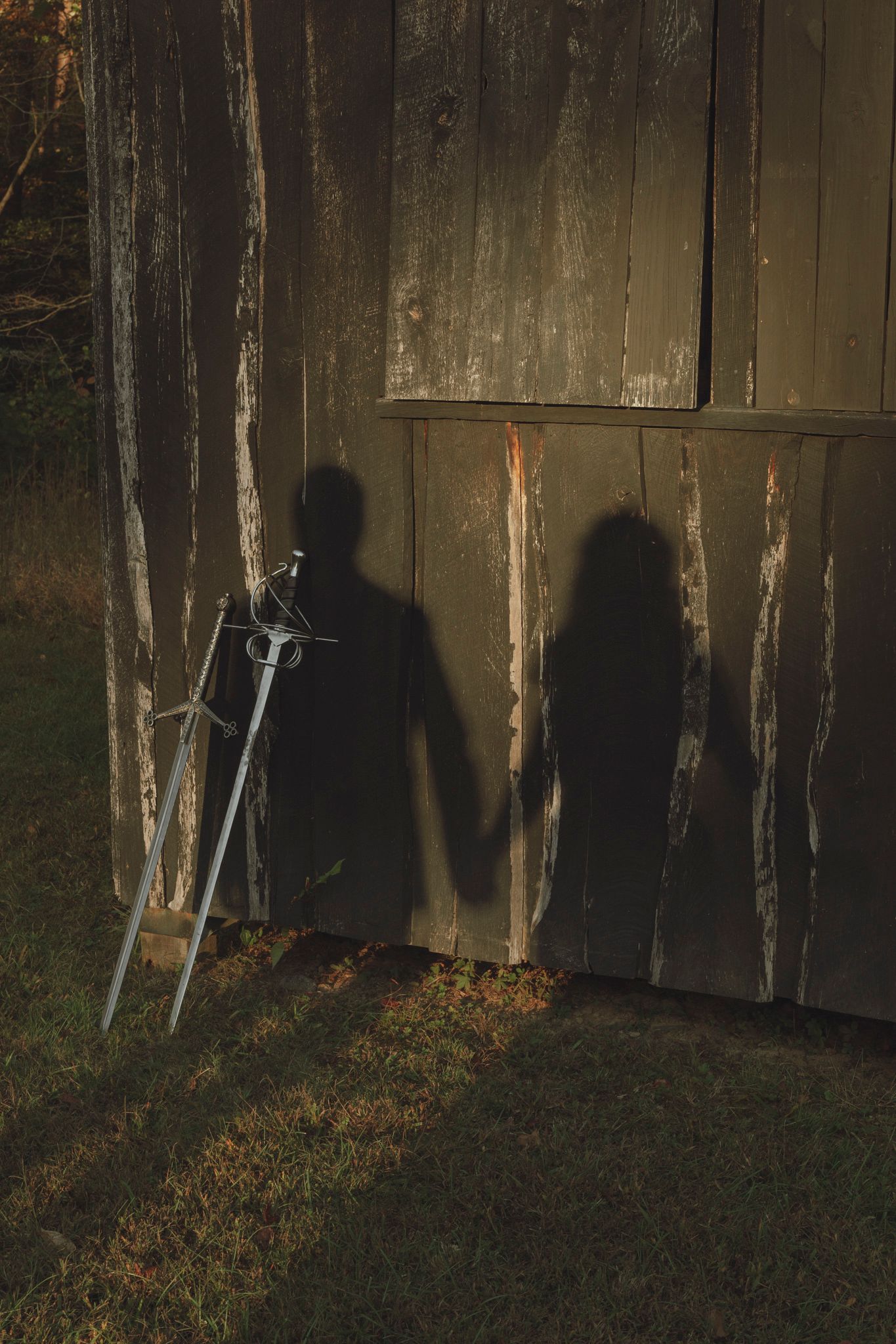 Dark shadows cast against a weathered wooden fence at dusk create an eerie silhouette effect in a backyard setting.