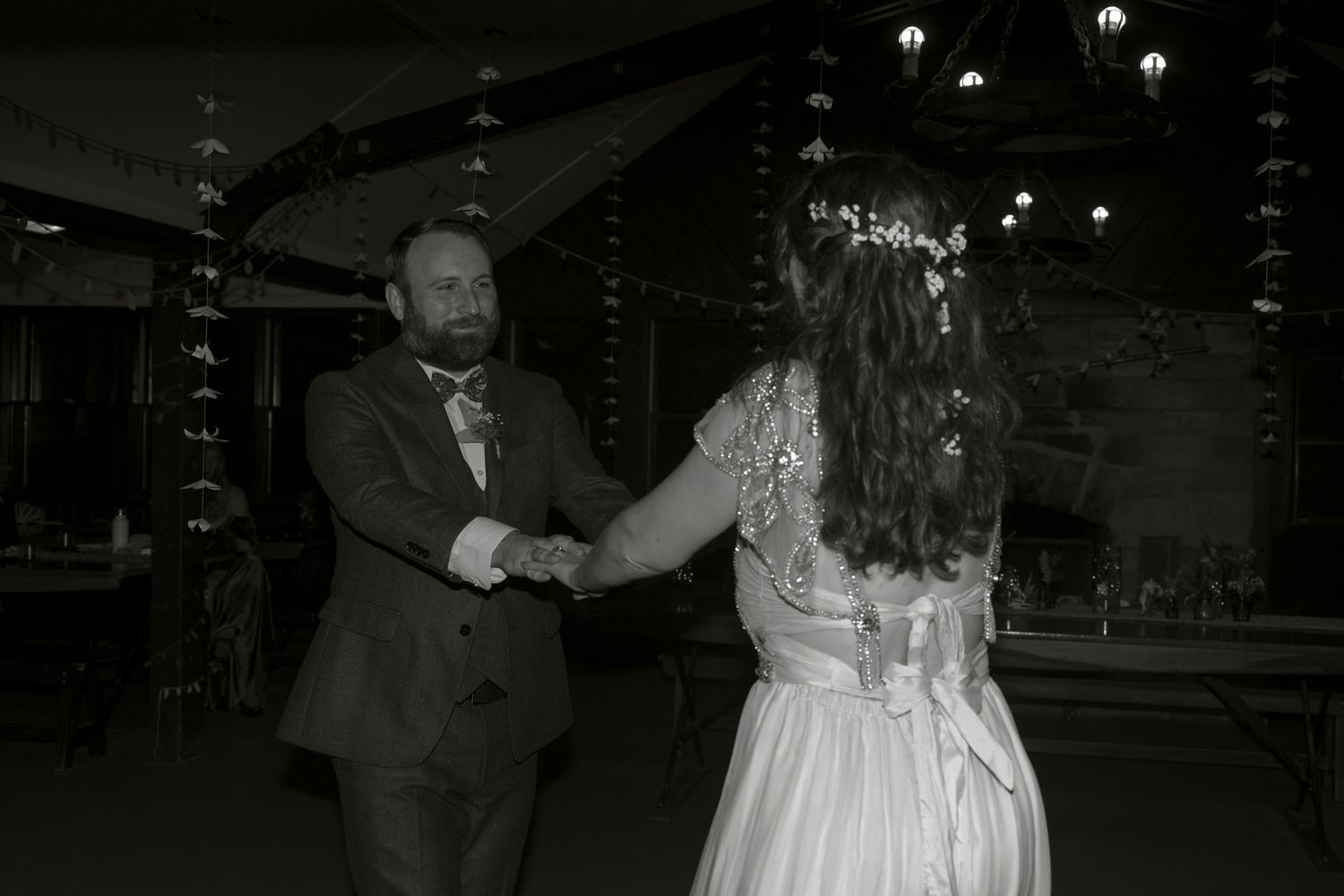 A couple dances together at a wedding reception, with the bride's white dress flowing gracefully across the dance floor.