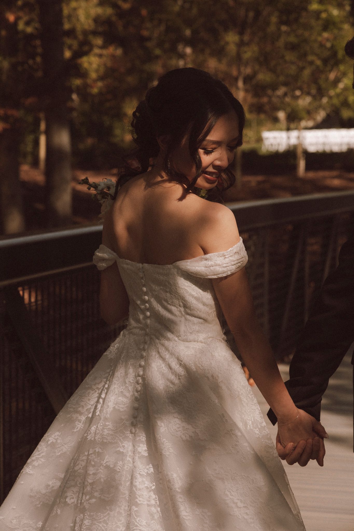 A wedding dress detail shot shows the intricate lace pattern and flowing fabric as a couple holds hands on a wooden deck.