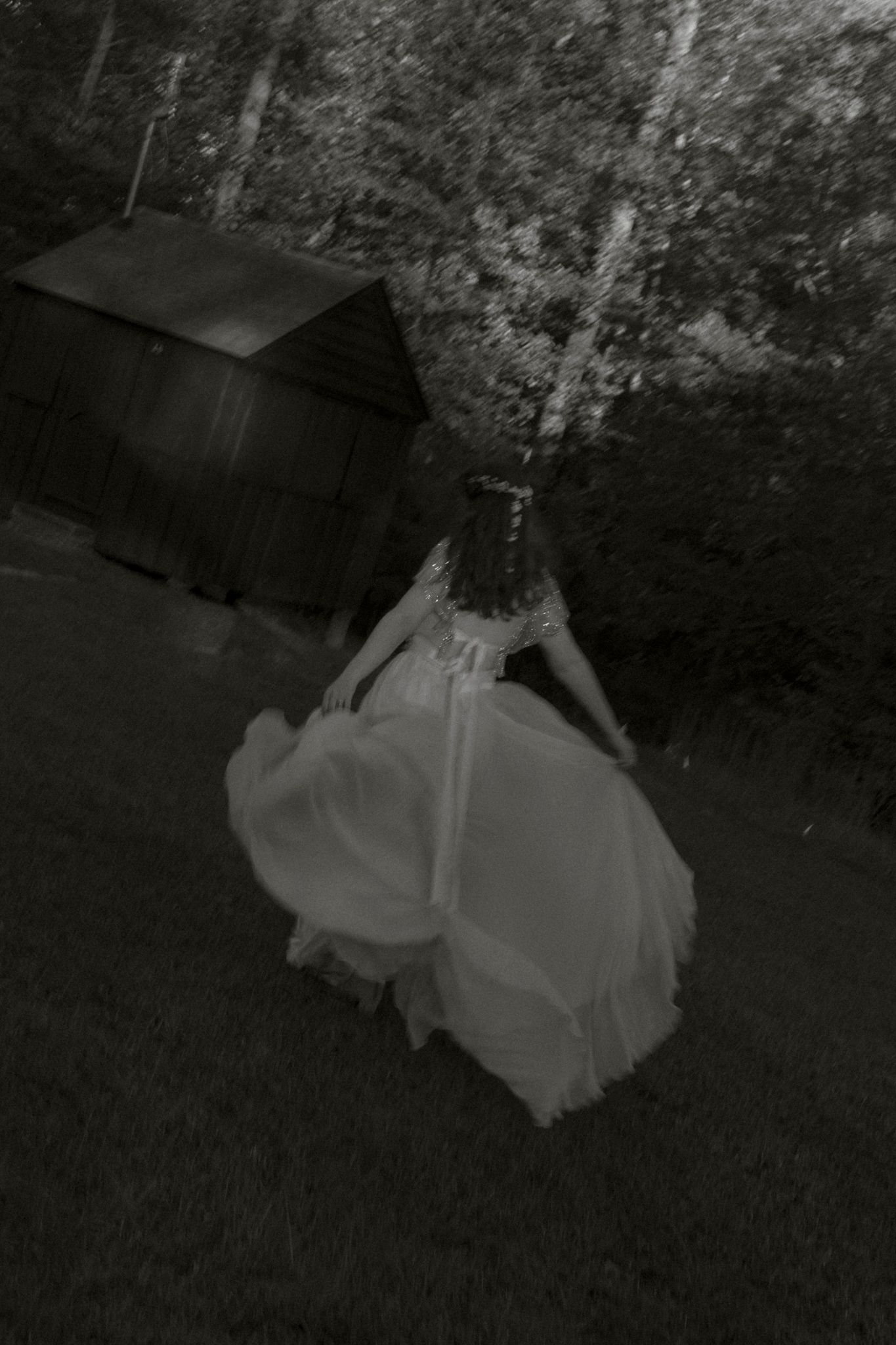 A sequence of dark, moody black and white photographs showing a figure in flowing white fabric moving through grass.