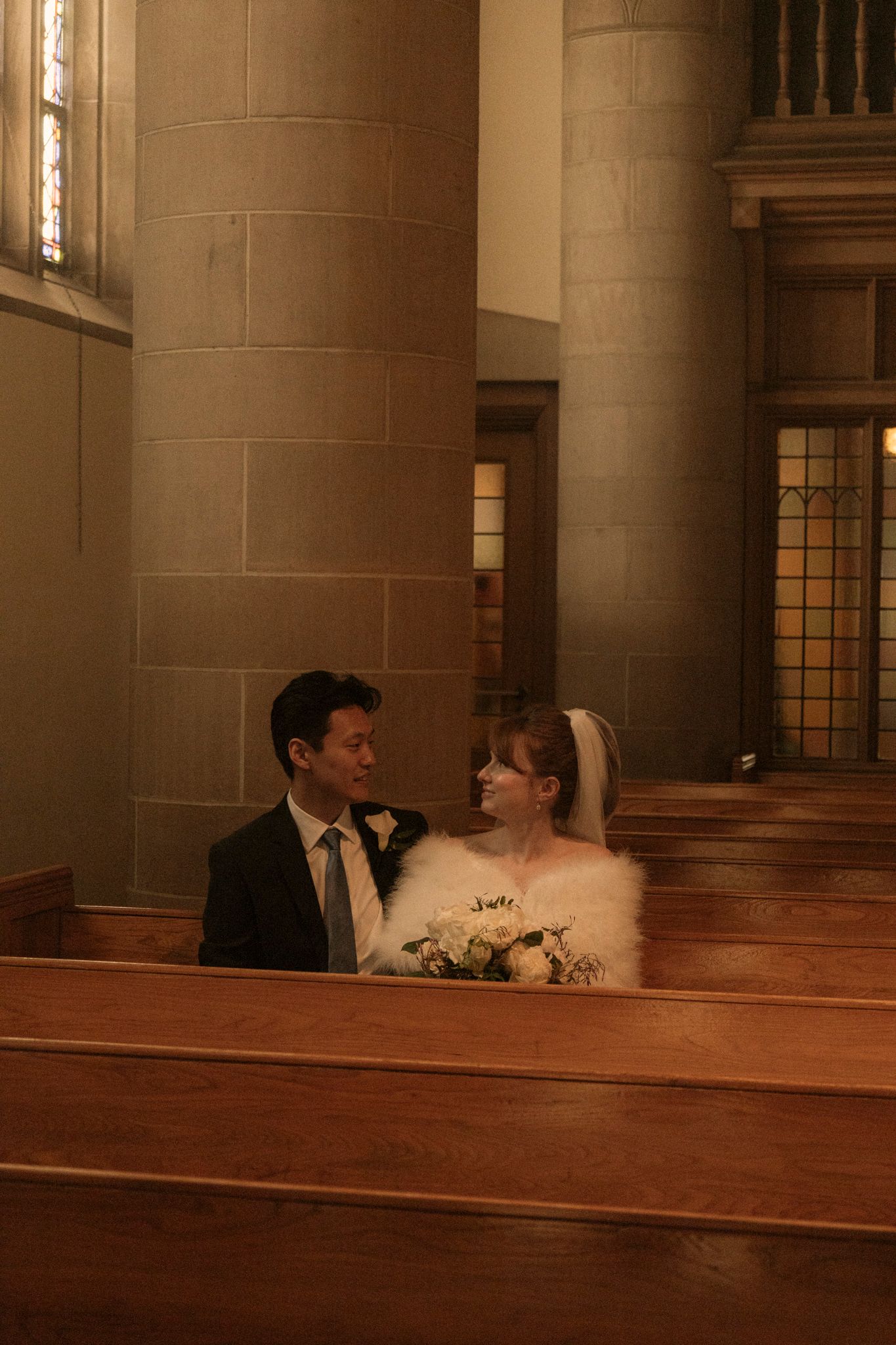 Bride and groom sitting together in wooden church pews, sharing a tender moment on their wedding day.