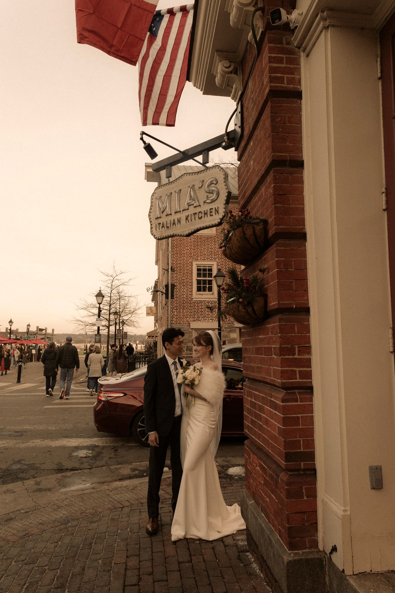 Bride and groom pose romantically outside Mila's Italian Kitchen on a brick street at dusk.