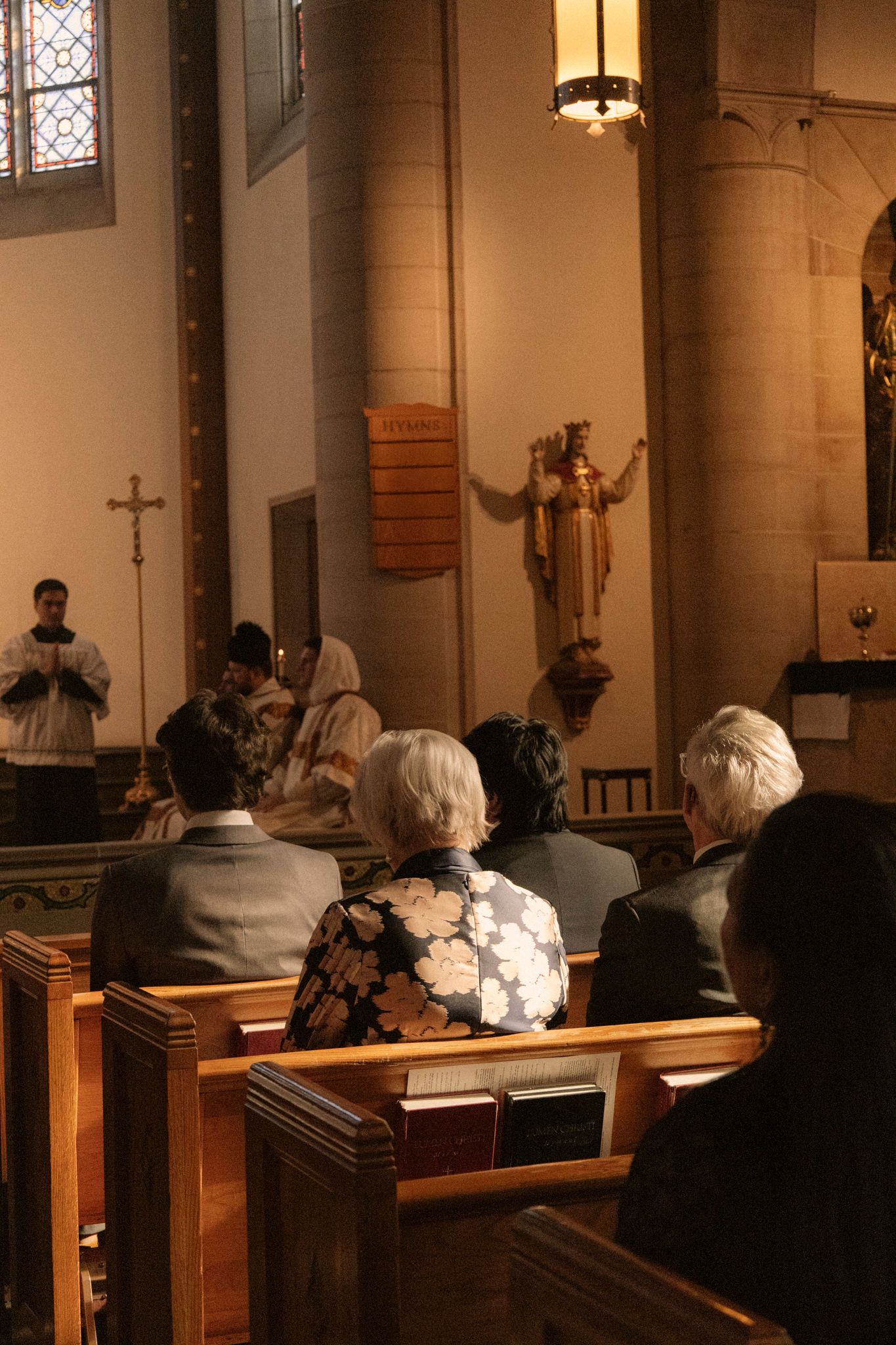 Wedding guests seated in wooden pews watching a Catholic wedding ceremony at a decorated altar.