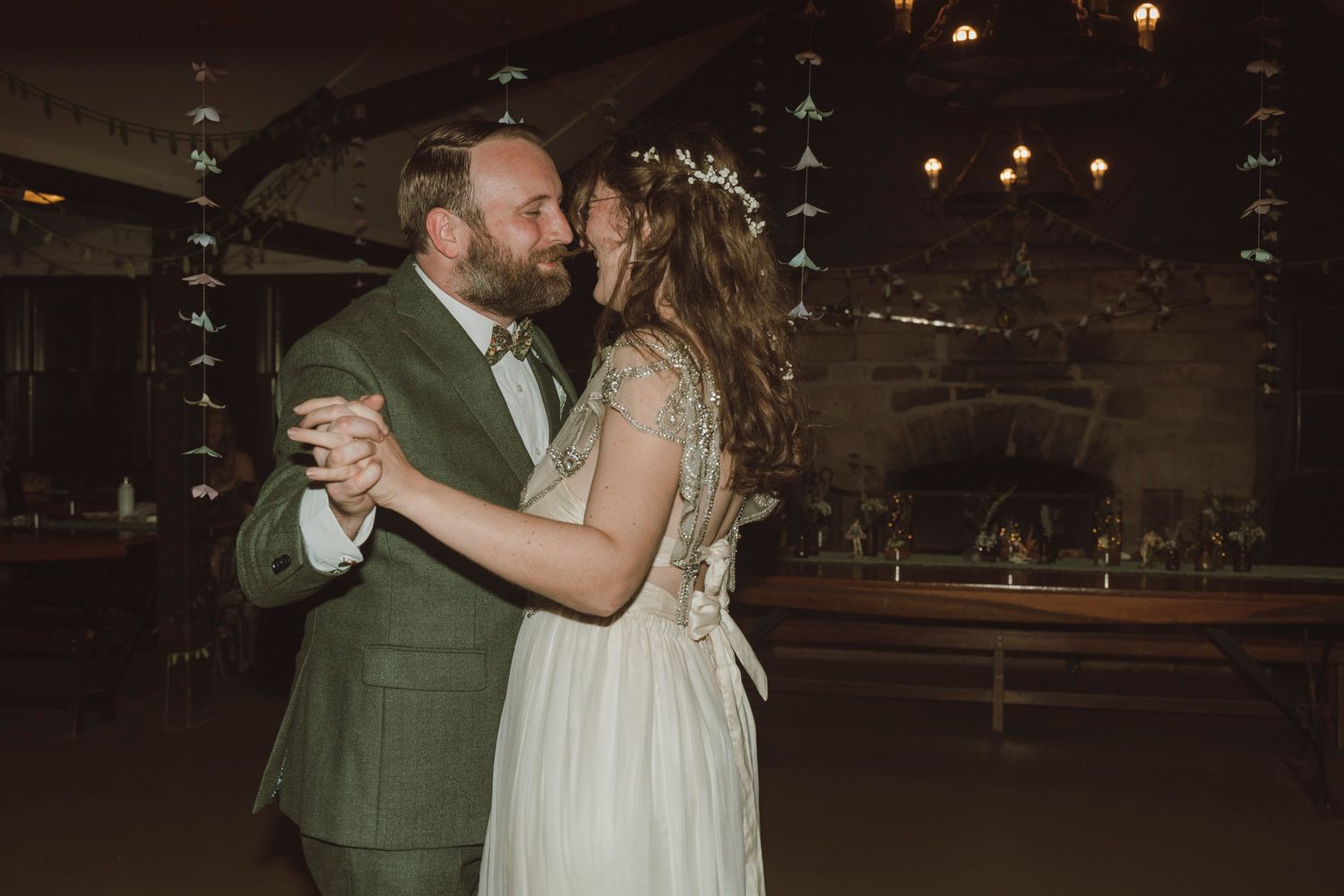A couple shares a romantic dance together during their wedding reception in a dimly lit rustic venue.
