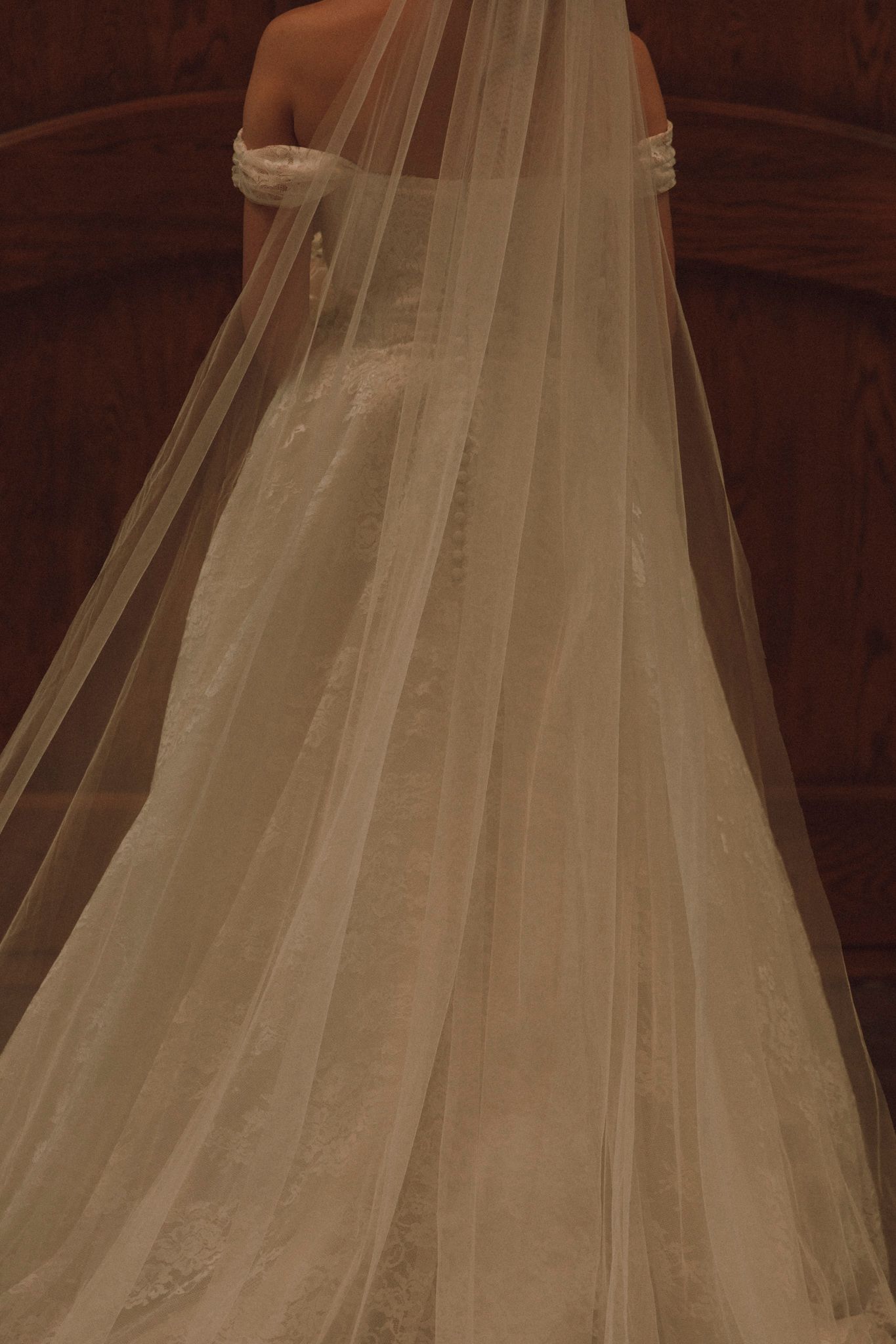 An elegant cathedral-length wedding veil trailing across dark hardwood flooring in warm lighting.